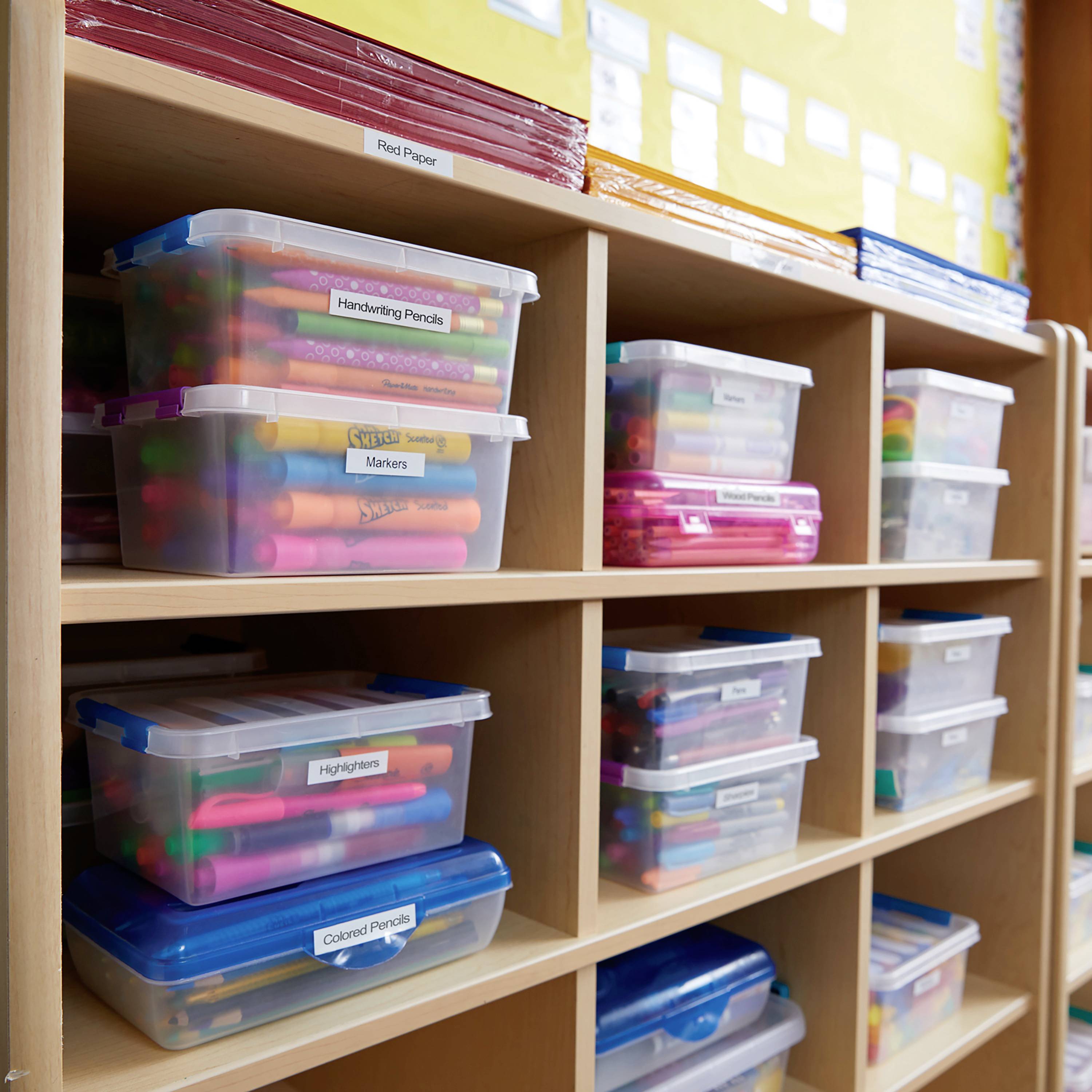Regale mit durchsichtigen Boxen voller bunter Marker und Stifte in einem Klassenzimmer. Boxen sind mit Etiketten beschriftet.