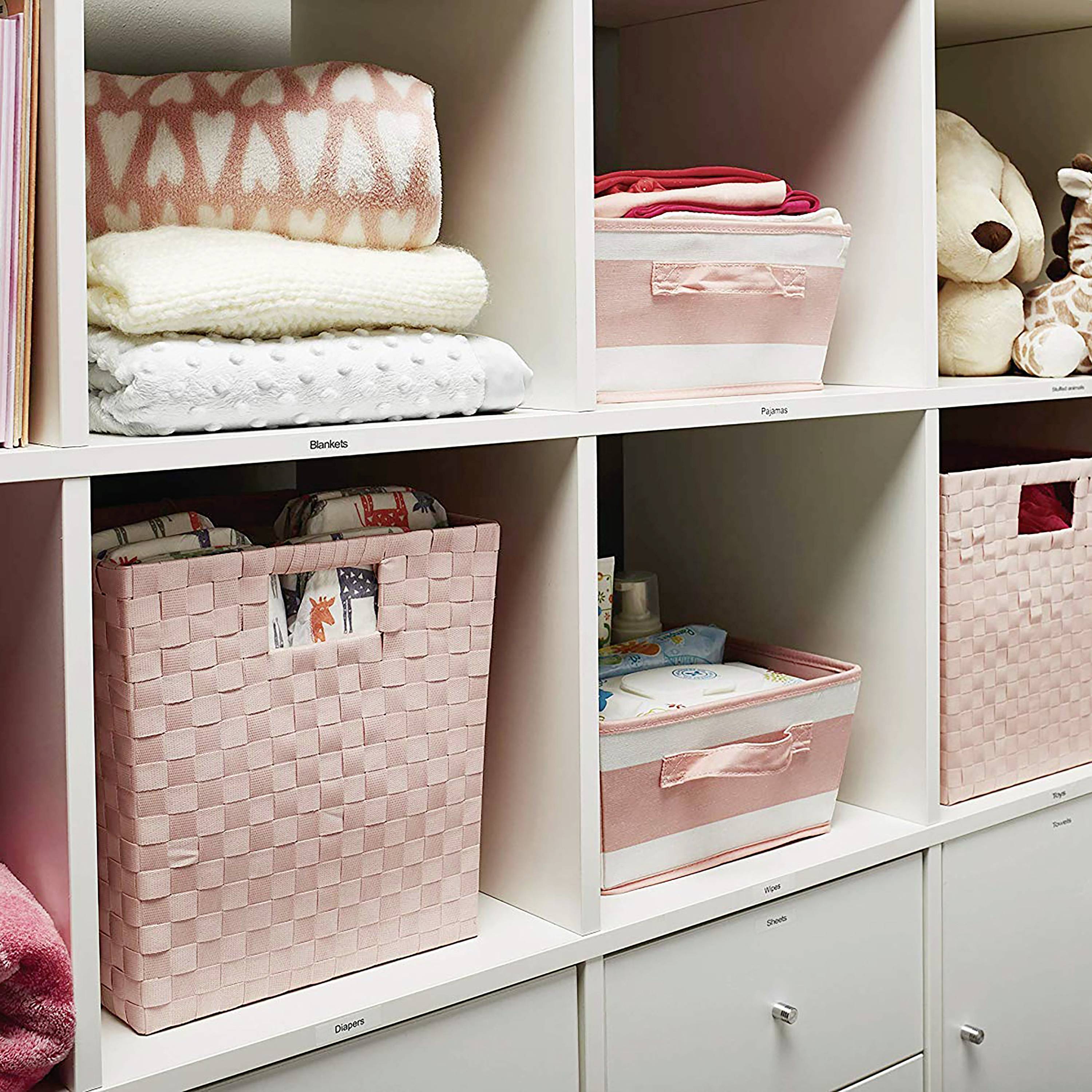 Regal mit rosa Aufbewahrungskörben und Spielzeug. Geordnet und dekorativ arrangiert, enthält Kleidung und Kuscheltiere.