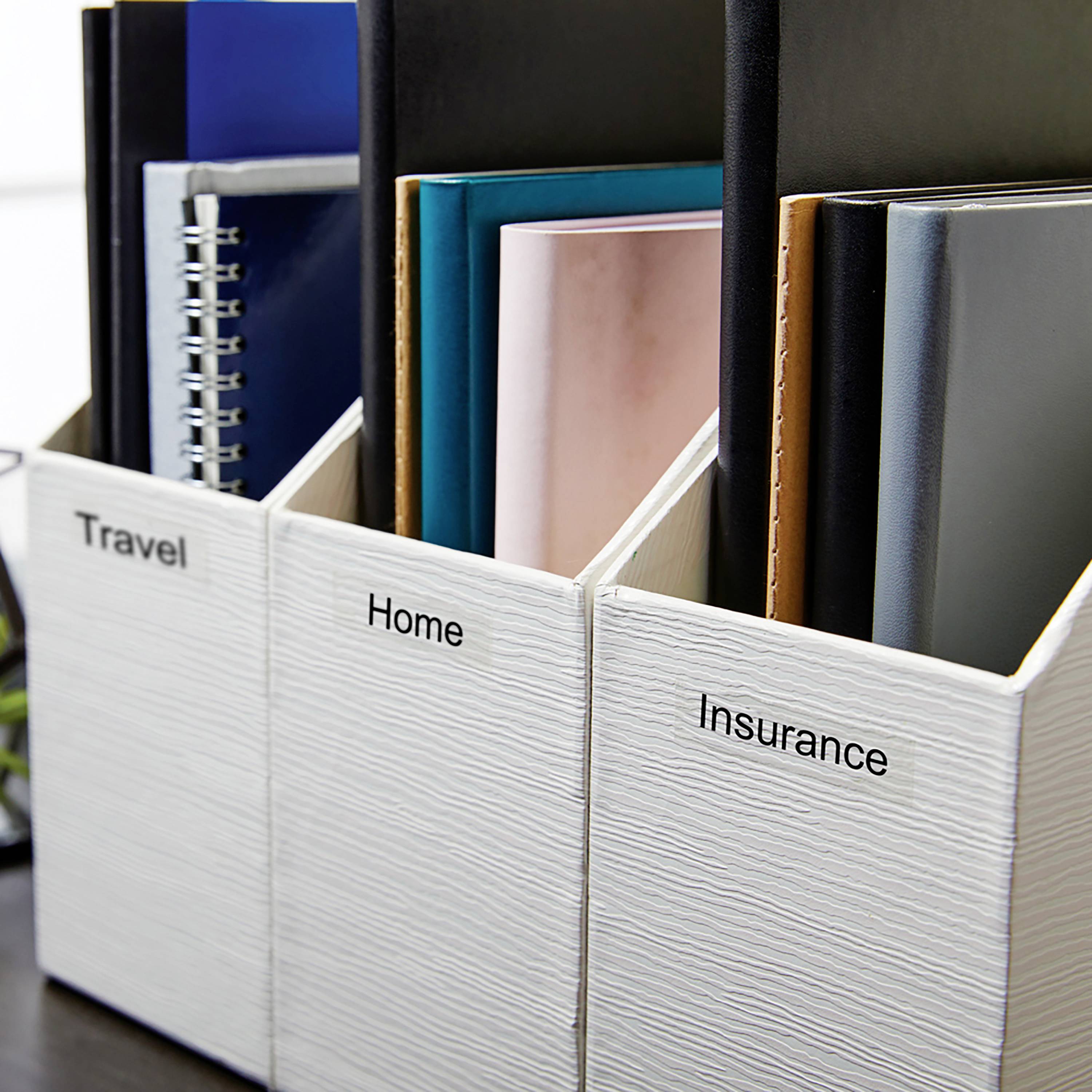 Drei weiße Zeitschriftenhalter auf einem Tisch, beschriftet mit 'Travel', 'Home' und 'Insurance'. Sie enthalten diverse Ordner und Dokumente.