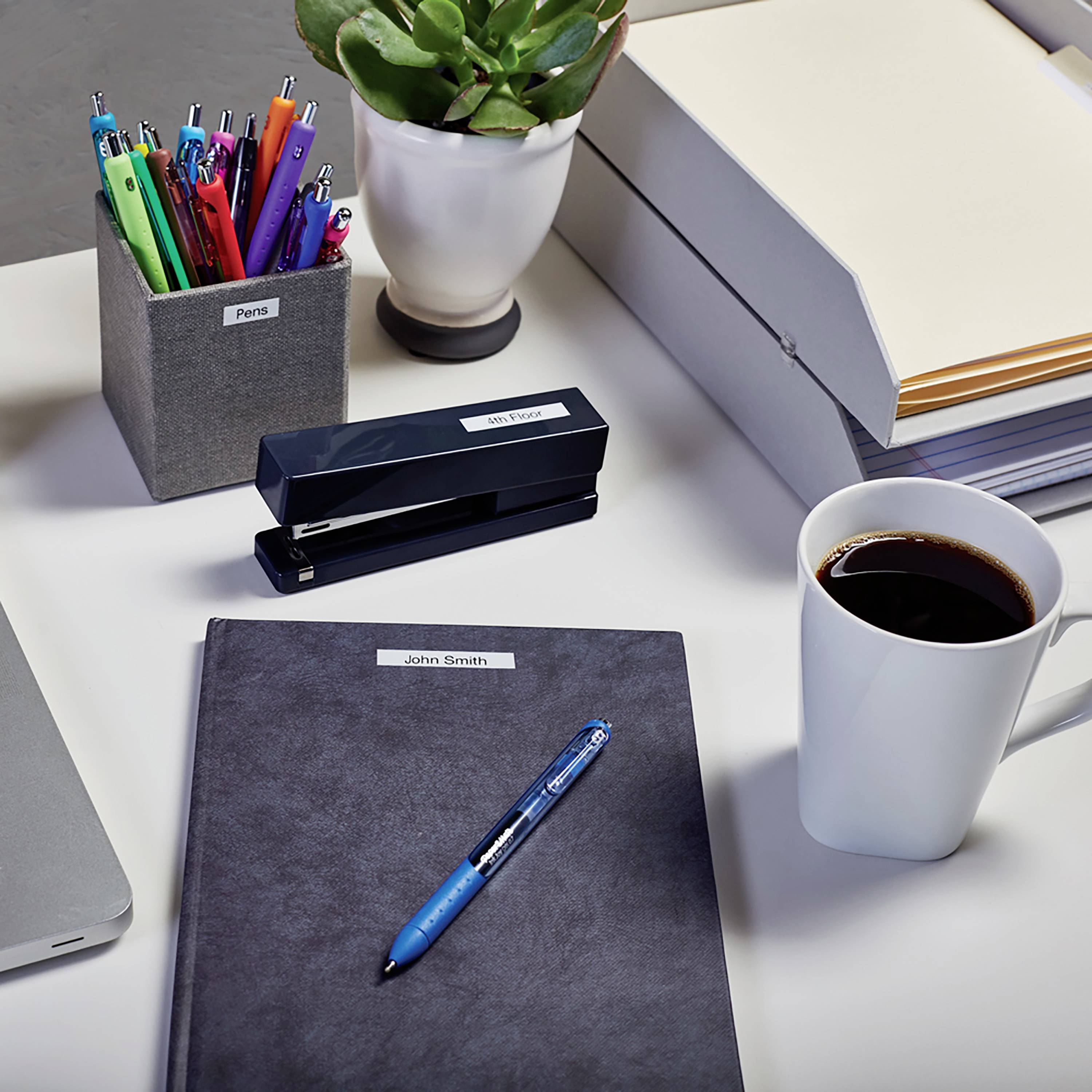 Ein Schreibtisch mit Stiften in einem Stiftehalter, einem Notizbuch, einer Tasse Kaffee, einem Hefter und Pflanzen im Hintergrund.