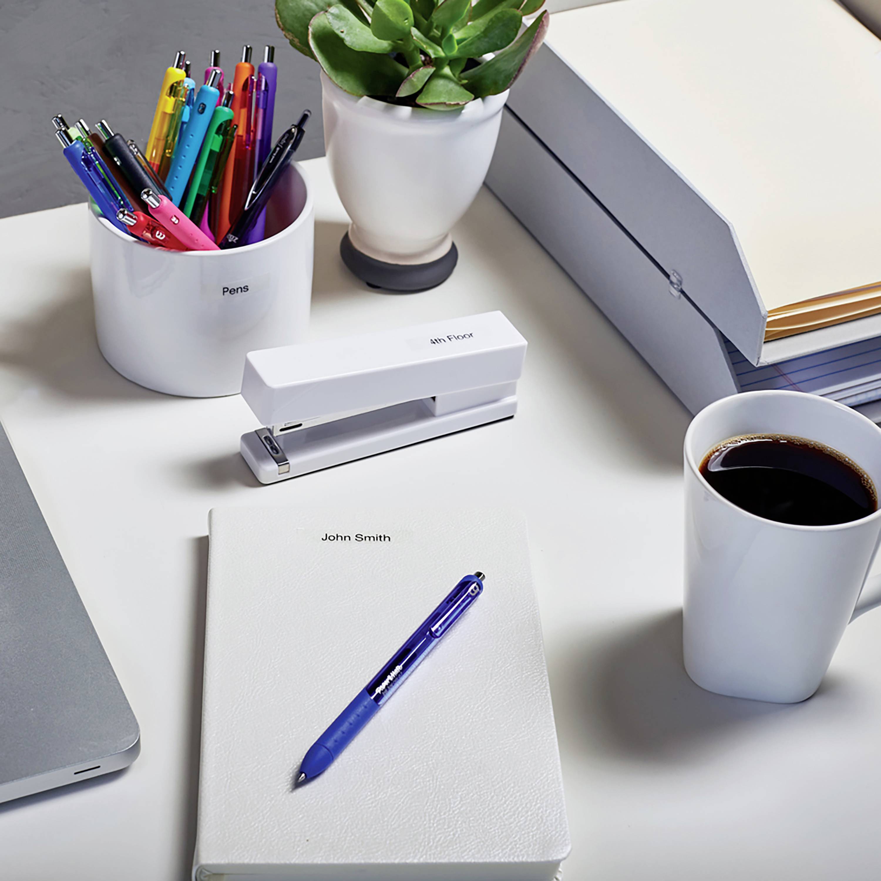 Schreibtisch mit Stiften, Notizzetteln, Pflanzen und einer Tasse Kaffee. Büromaterial ordnet sich um einen Laptop.