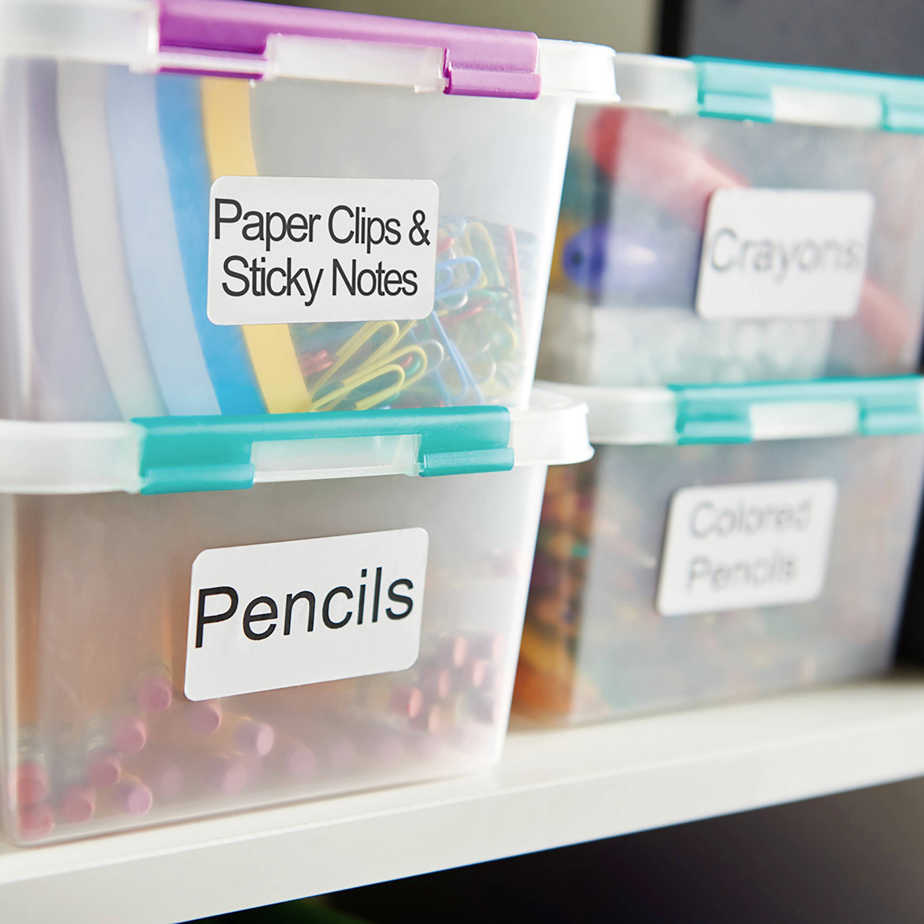 Drei Kunststoffboxen auf einem Regal, beschriftet mit 'Paper Clips & Sticky Notes', 'Pencils' und 'Colored Pencils', mit farbigem Inhalt.