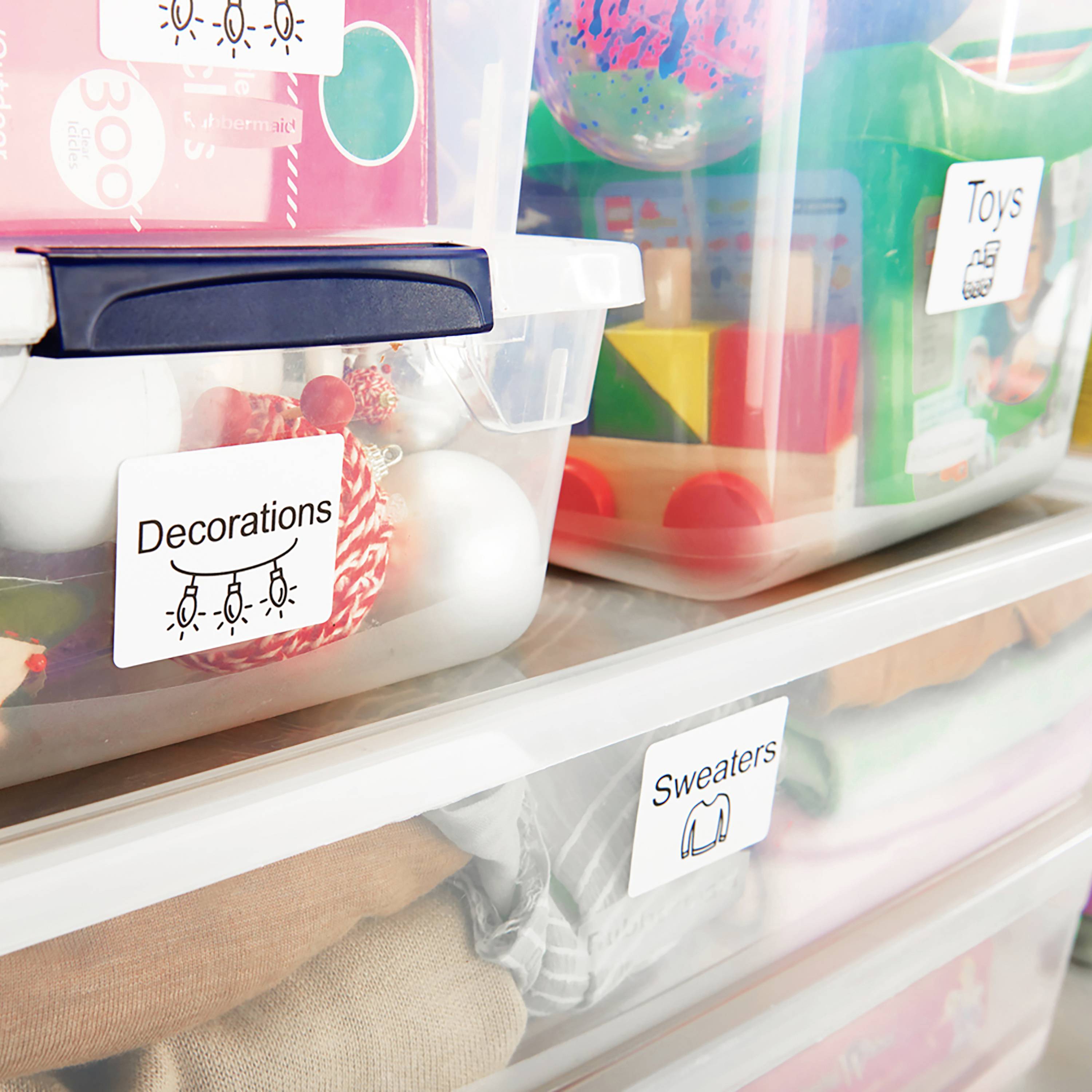 Plastikboxen mit Etiketten 'Decorations', 'Toys' und 'Sweaters', die verschiedene Gegenstände zur Aufbewahrung im Regal zeigen.