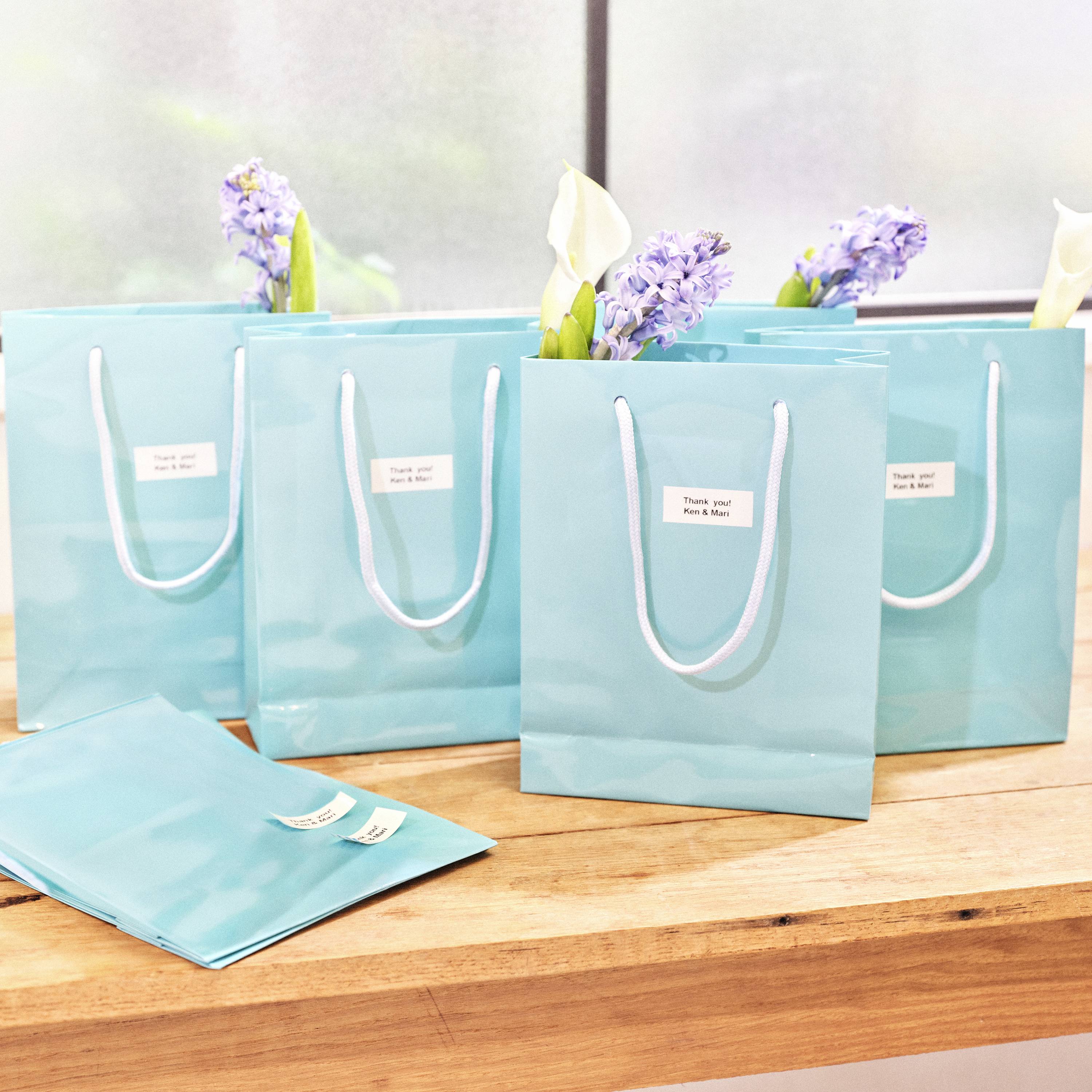 Türkise Geschenktüten mit Blumen dekoriert, auf Holztisch in heller Umgebung.