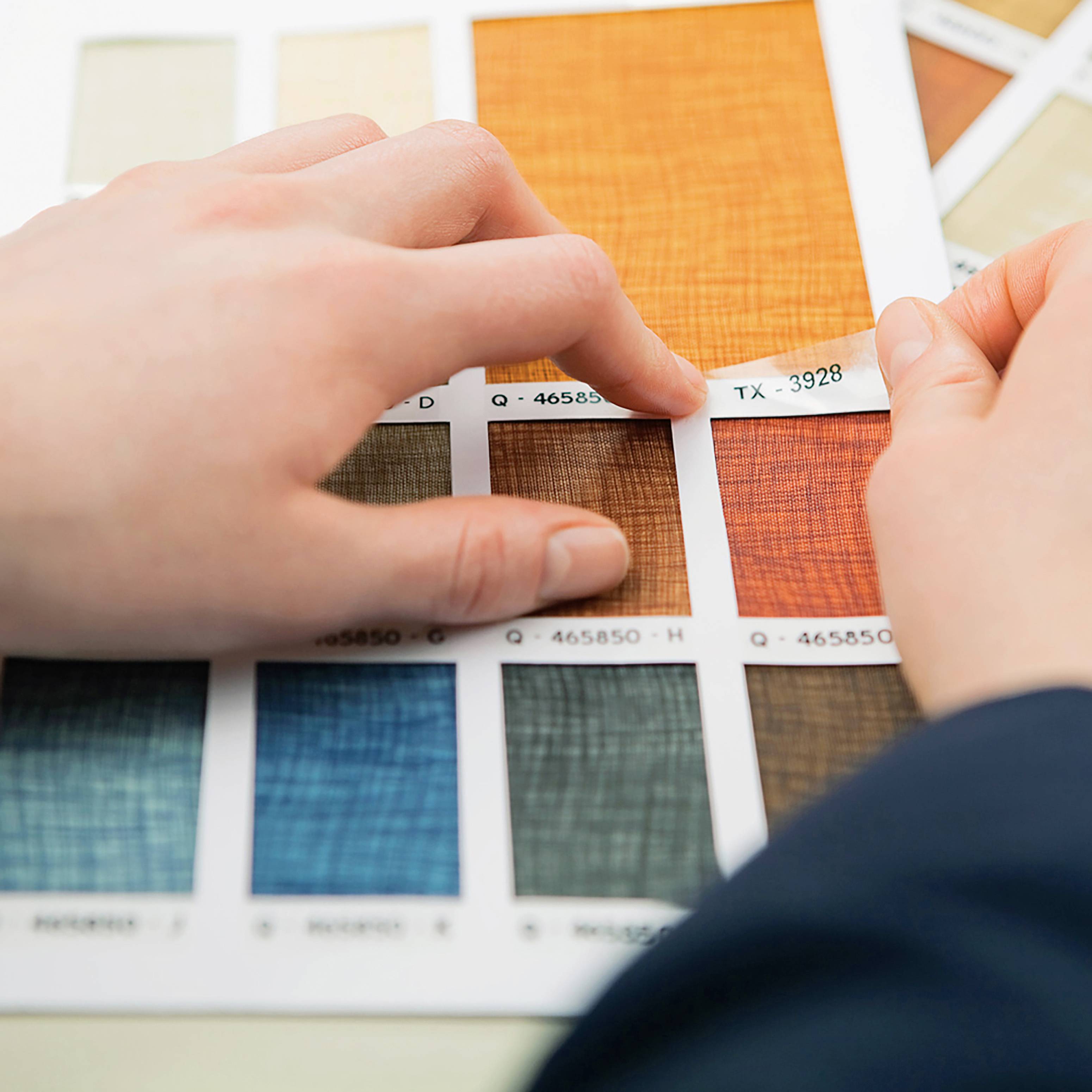 Person zeigt auf eine Farbpalette mit Stoffmustern, wobei ein orangefarbenes Muster im Fokus ist.