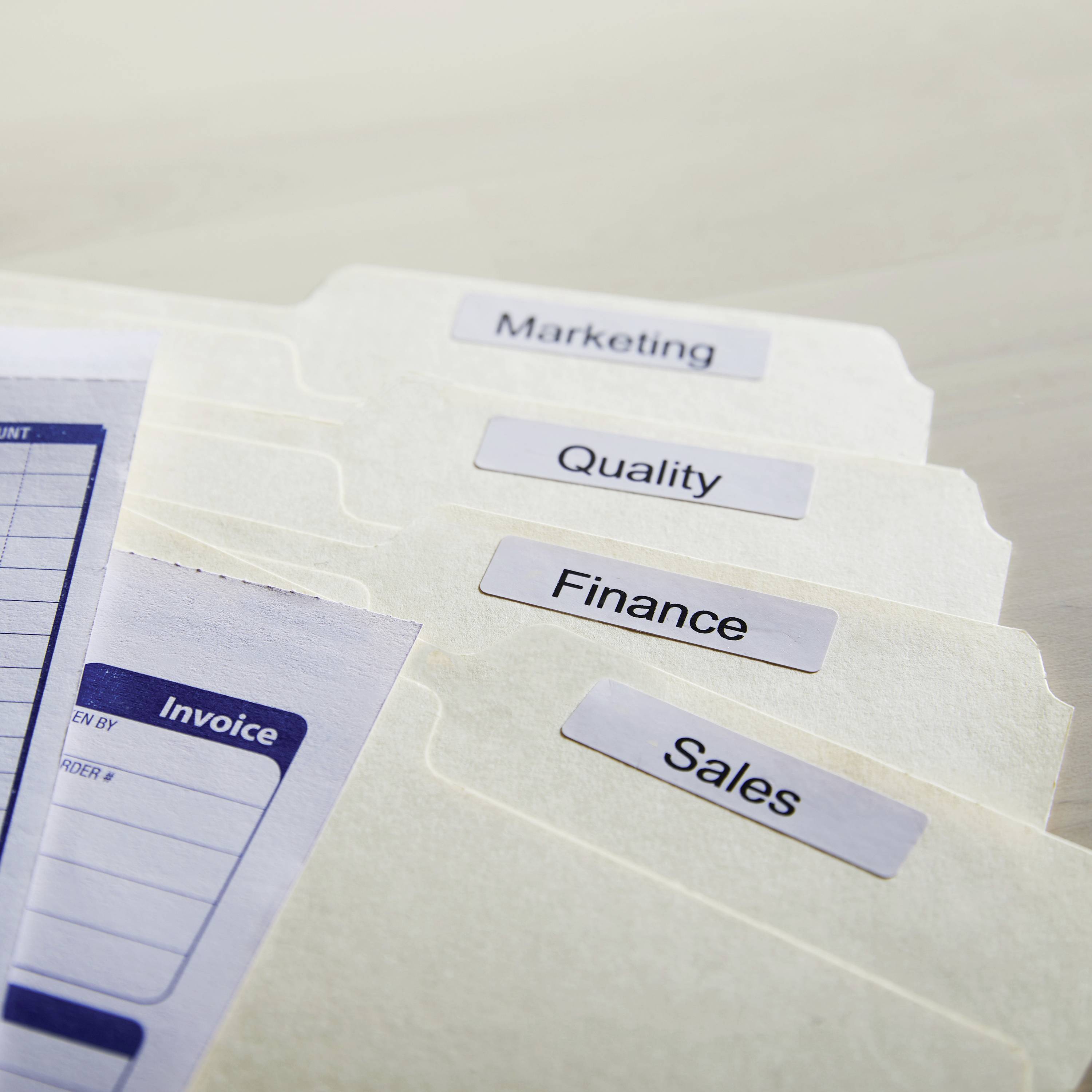 Ordnerregister mit den Beschriftungen 'Marketing', 'Quality', 'Finance' und 'Sales' auf einem Schreibtisch.