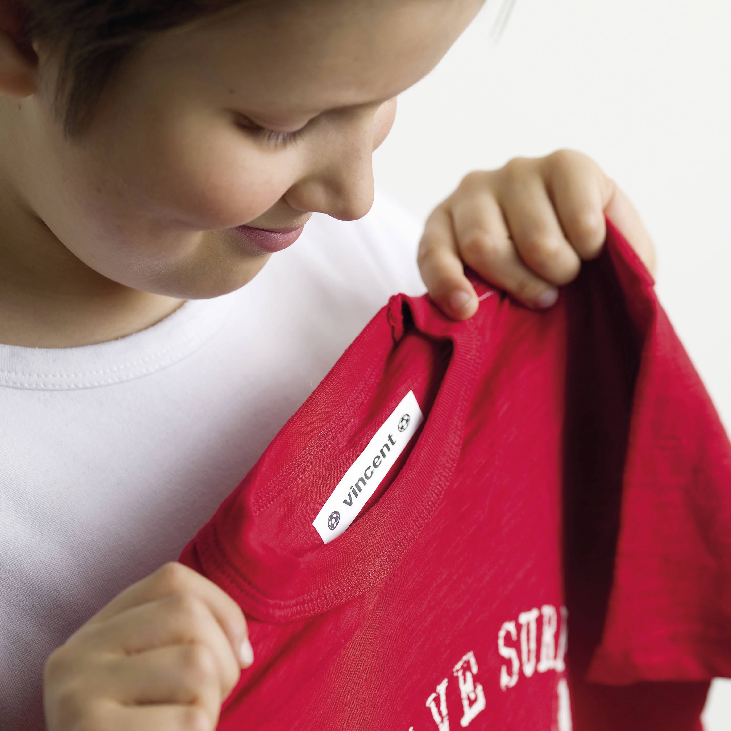 Ein Kind hält ein rotes T-Shirt mit dem Label 'Vincent'. Es scheint neugierig und konzentriert zu schauen.