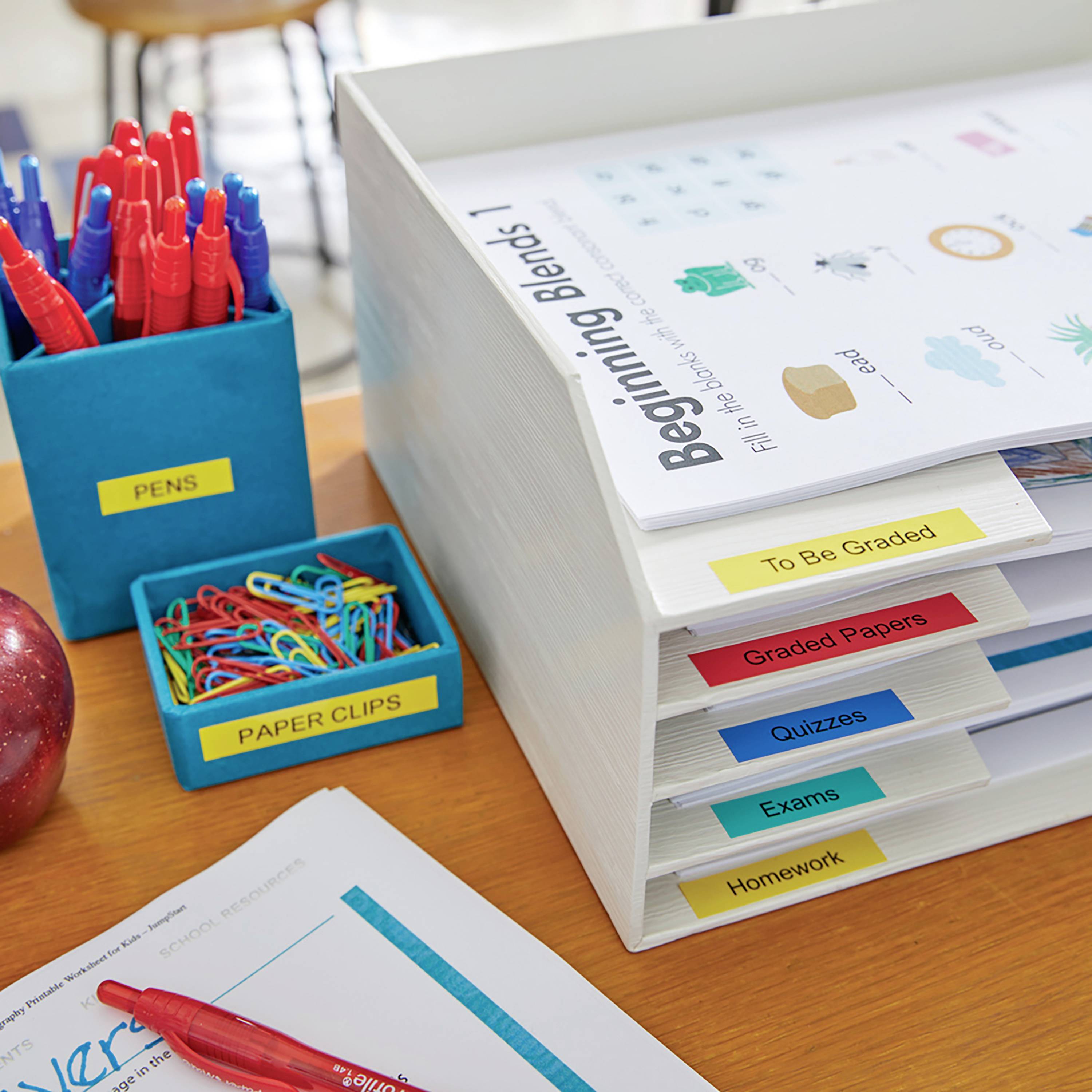 Büroarbeitsbereich mit Aktenordnern, beschriftet mit ’Graded Papers’, ’Exams’, ’Quizzes’ und ’Homework’. Stifte und Büroklammern in Haltern.