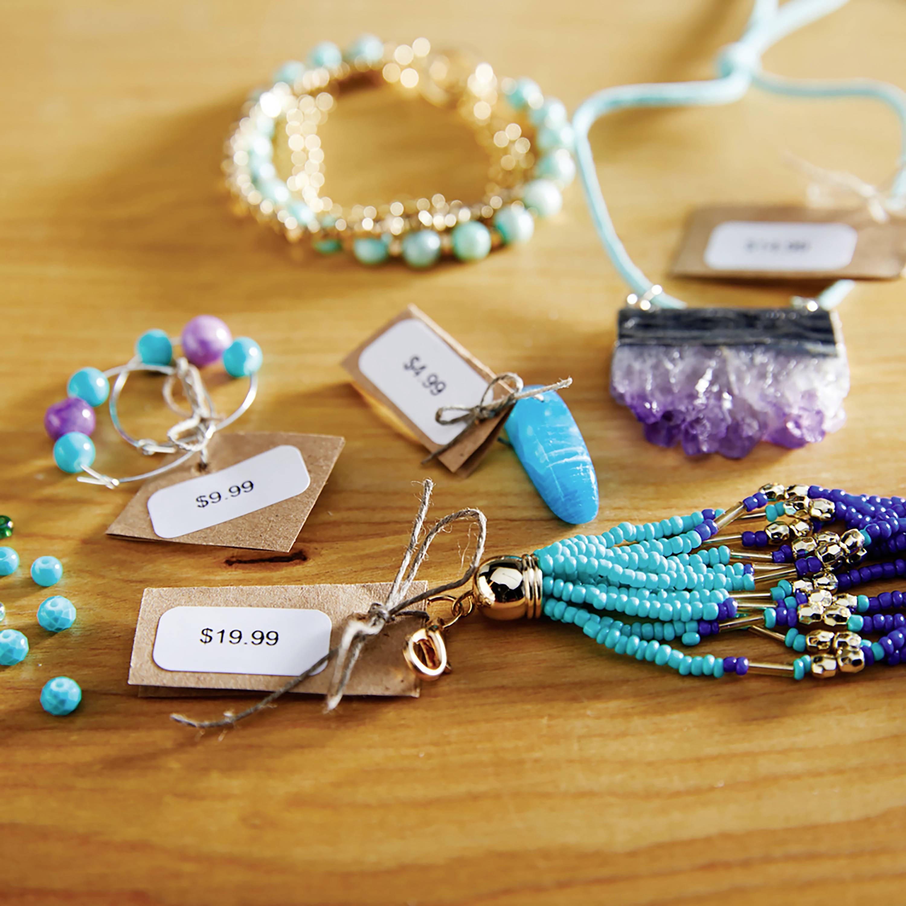 Schmuck auf Holztisch: Türkise und violette Perlen, Armbänder, Ohrringe mit Preisschildern '19.99 $', '8.95 $', '9.99 $'.