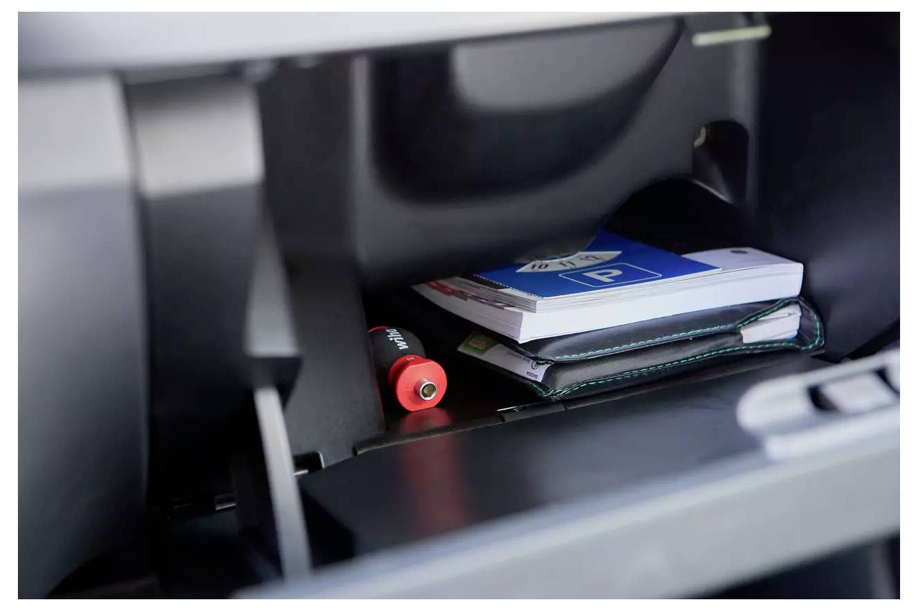 In einem Handschuhfach eines Autos befinden sich eine Parkerlaubnis, eine AAA-Batterie und eine Bedienungsanleitung.