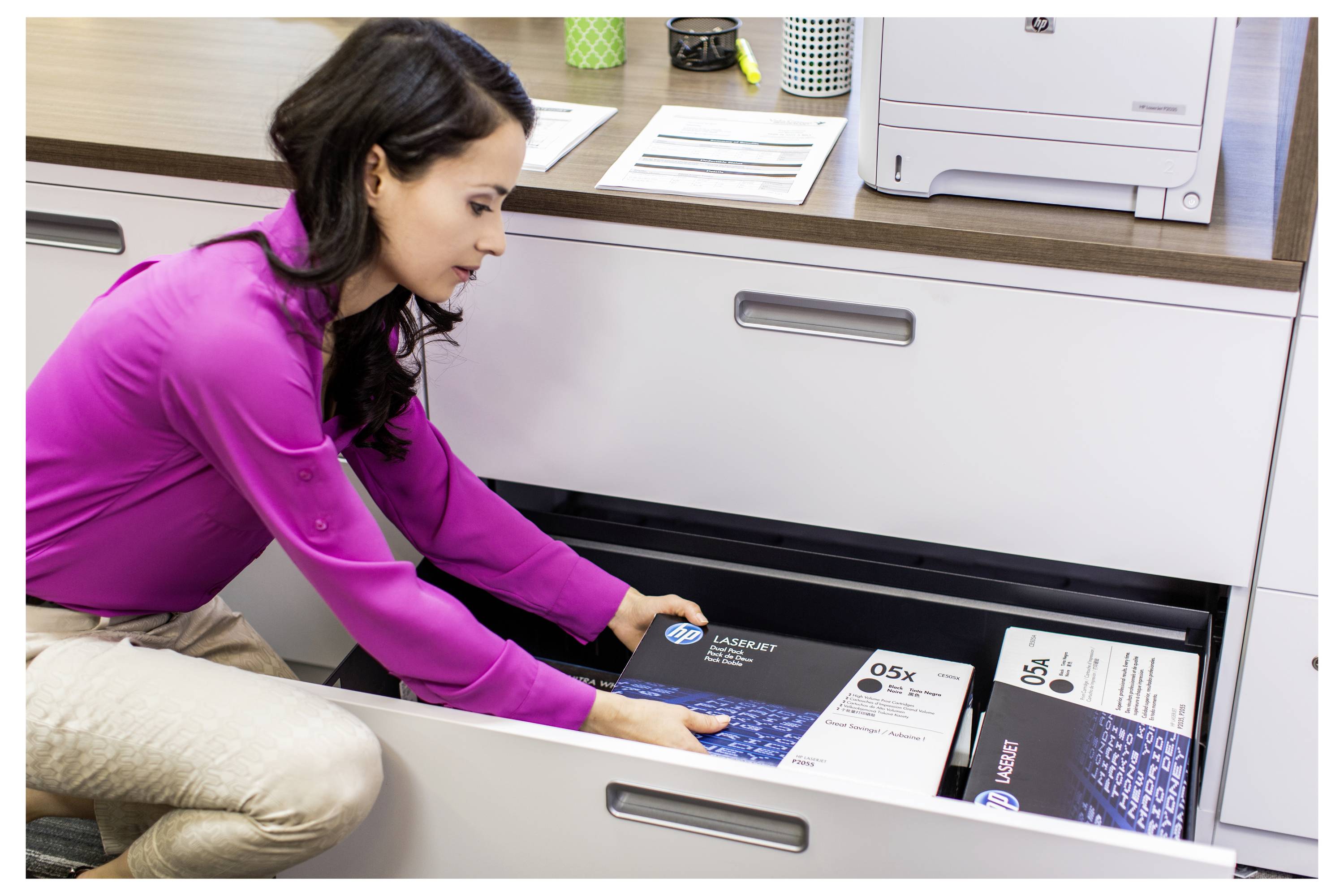 Frau kniet neben einer offenen Schreibtischschublade und stellt HP LaserJet Druckerpapierkartons in den Stauraum unter einem Schreibtisch.