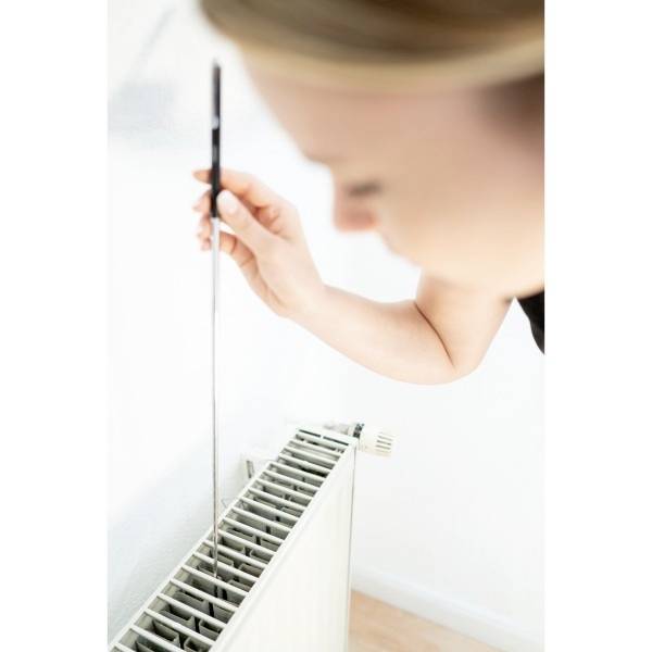 Eine Person entlüftet einen Heizkörper mit einem Entlüftungsschlüssel. Der Heizkörper befindet sich an einer weißen Wand.