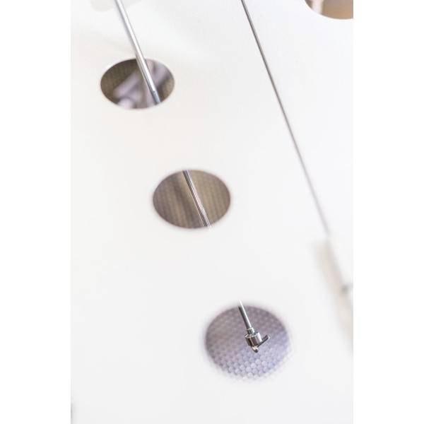 Drei runde Öffnungen in einer weißen Oberfläche, mit dahinterliegenden metallischen Elementen und einem radialen Muster.