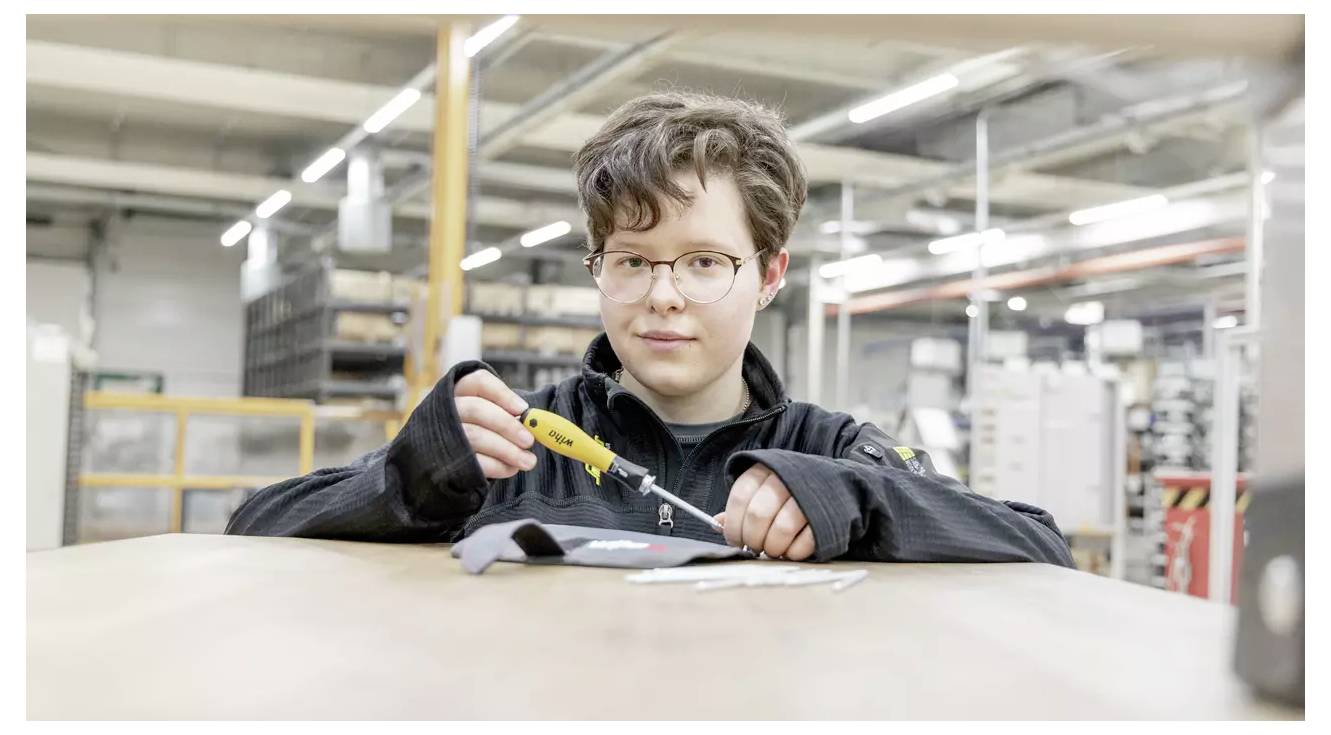 Eine Person, die ein tragbares Werkzeug auf einem Stoffstück in einer industriellen Umgebung verwendet und sich auf Detailarbeit konzentriert.