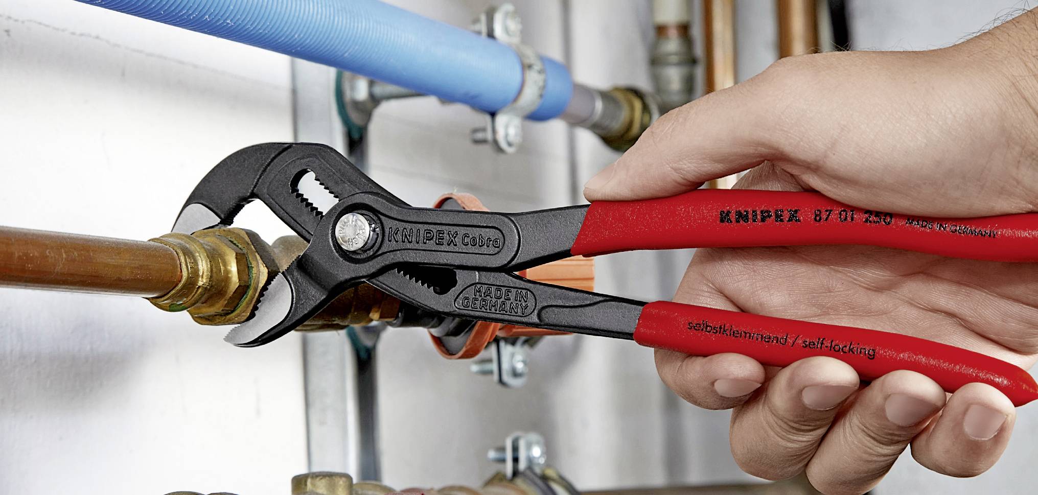 Eine Hand hält eine rote Wasserpumpenzange, die ein Rohr in einem Installationssystem festzieht.