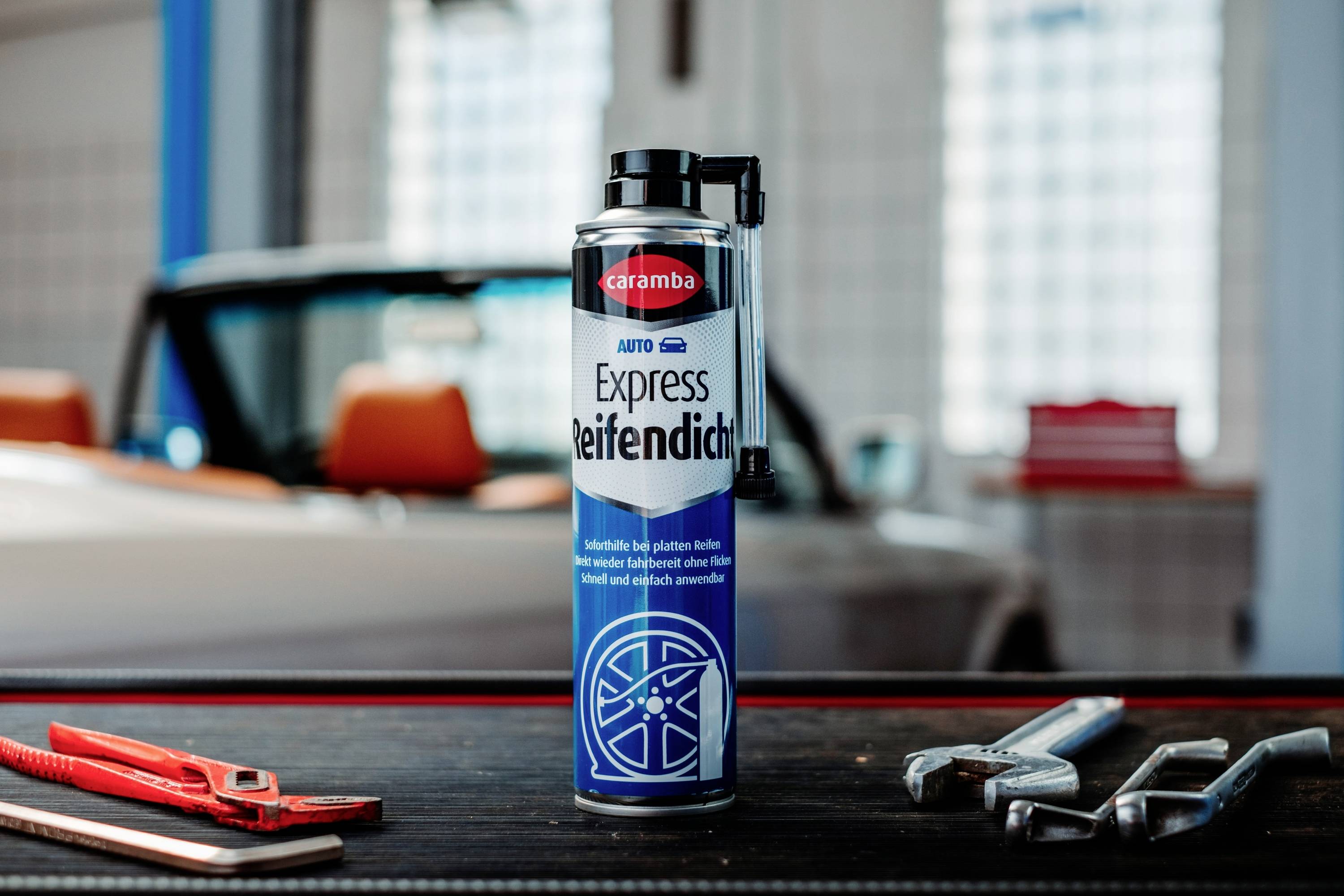 Eine Dose 'Caramba Express Reifendicht', ein Reifendichtungsmittel, auf einem Tisch mit Schraubenschlüsseln und Zangen, ein unscharfer Oldtimer im Hintergrund.