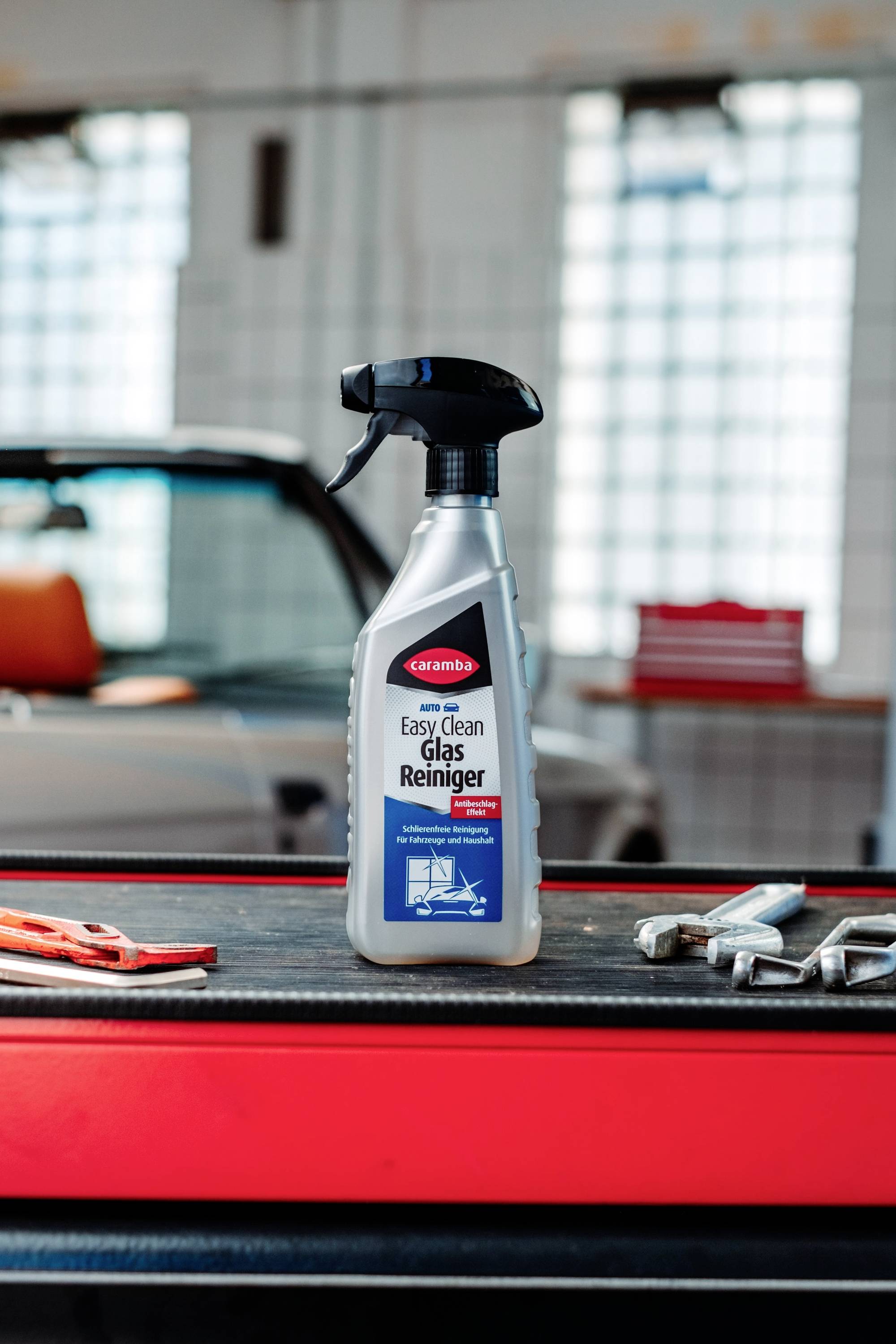 Eine Flasche 'Easy Clean Glas Reiniger' Reinigungsspray auf einer Oberfläche in einer Garagenumgebung, mit einem Auto und Werkzeugen im Hintergrund.