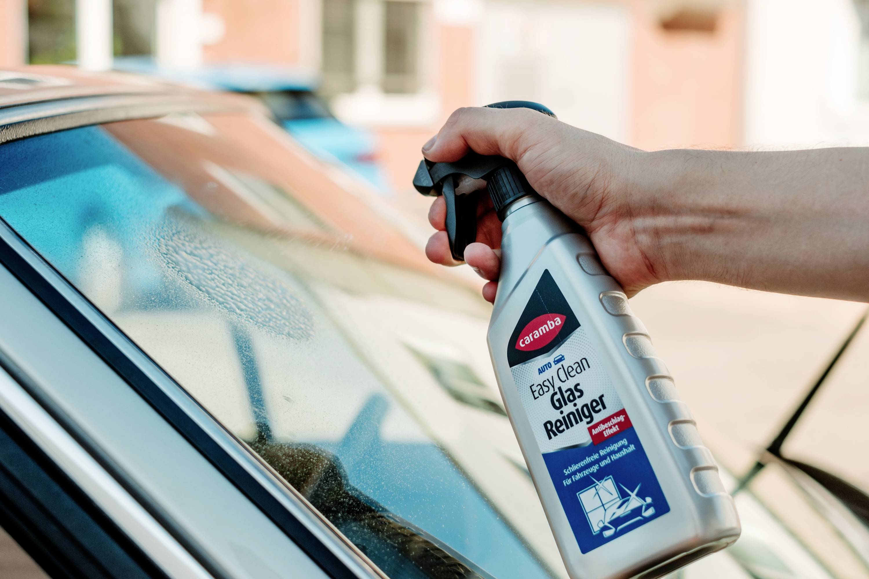 Eine Hand sprüht Glasreiniger aus einer Flasche mit der Aufschrift 