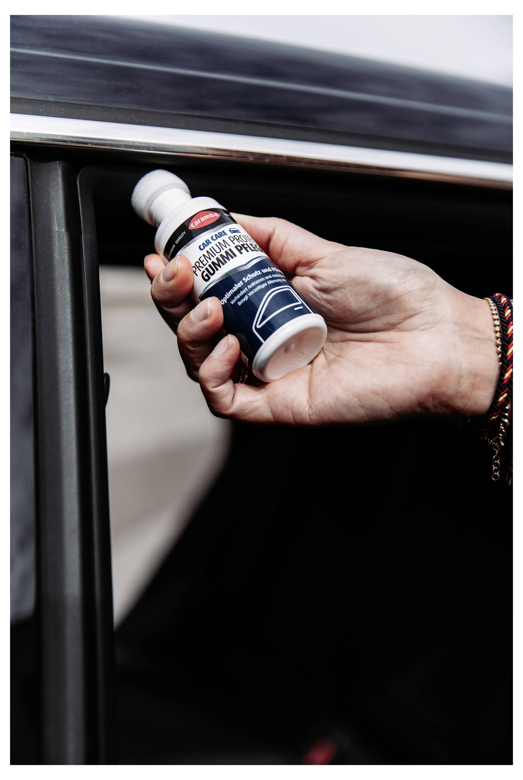 Hand holding a bottle of 'GUMMI PREP' cleaner beside a car door, suggesting application to vehicle trim or paint repair