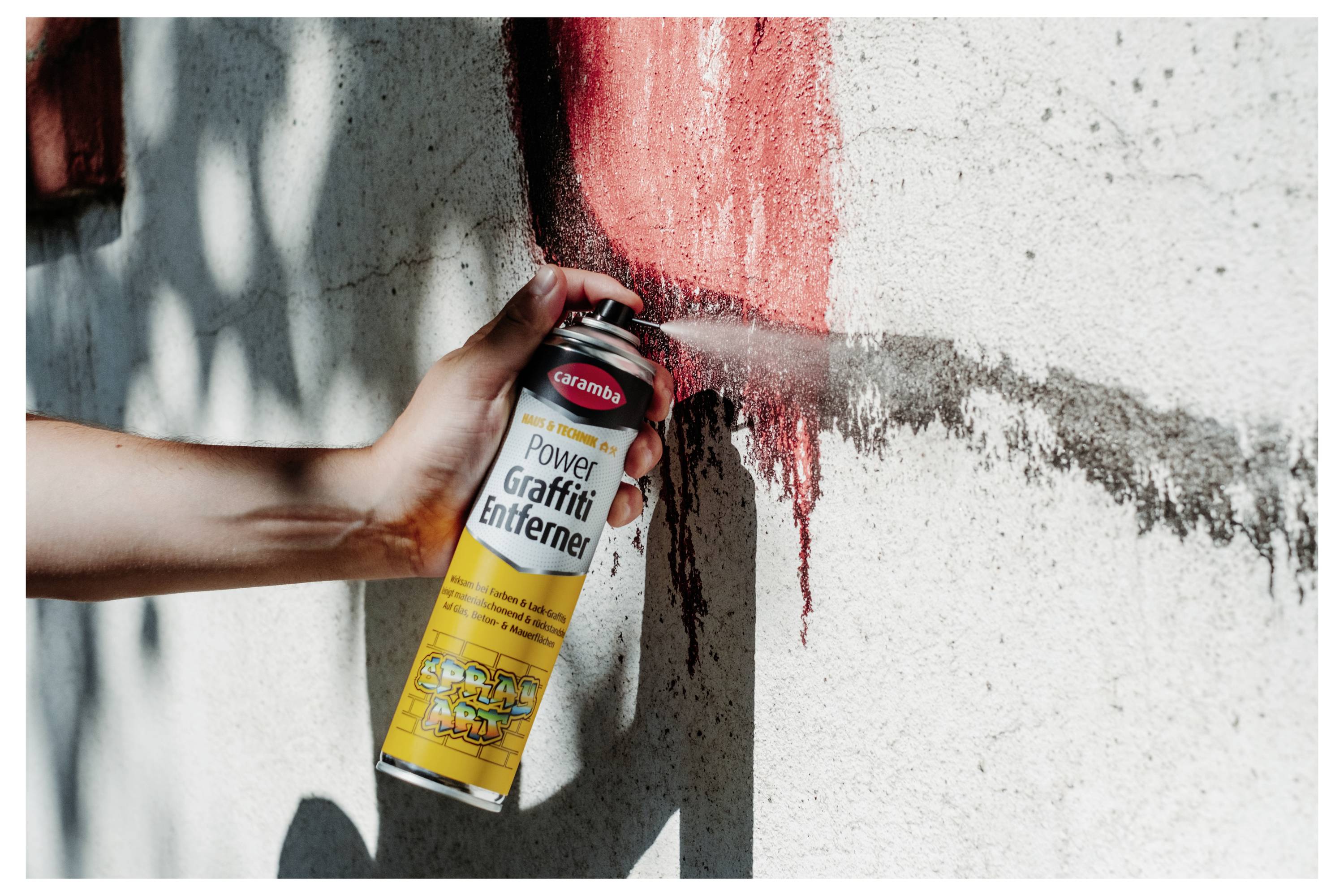 Eine Hand sprüht Graffiti-Entferner aus einer Dose mit der Aufschrift 
