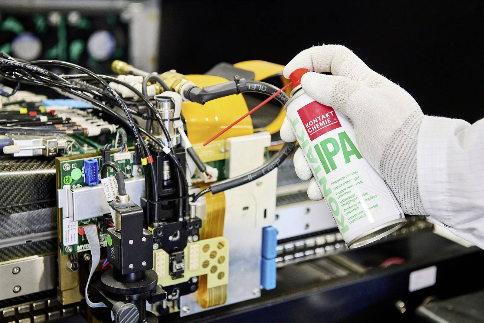 Nahaufnahme von einem Mikrochip, der mit einem Reinigungsspray bearbeitet wird, das von einer Person mit weißen Handschuhen verwendet wird.