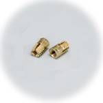 Zwei kleine, zylindrische Metallteile mit geriffelter Oberfläche liegen nebeneinander auf einer hellen Oberfläche.