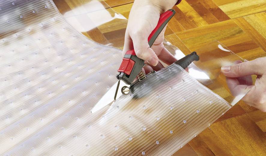 Eine Person schneidet eine transparente Kunststofffolie mit einer Schere auf einem Holzboden.