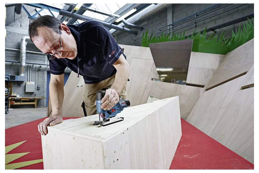 Ein Mann benutzt eine Stichsäge, um einen großen Holzblock in einer Werkstatt oder einem industriellen Testbereich zu schneiden.