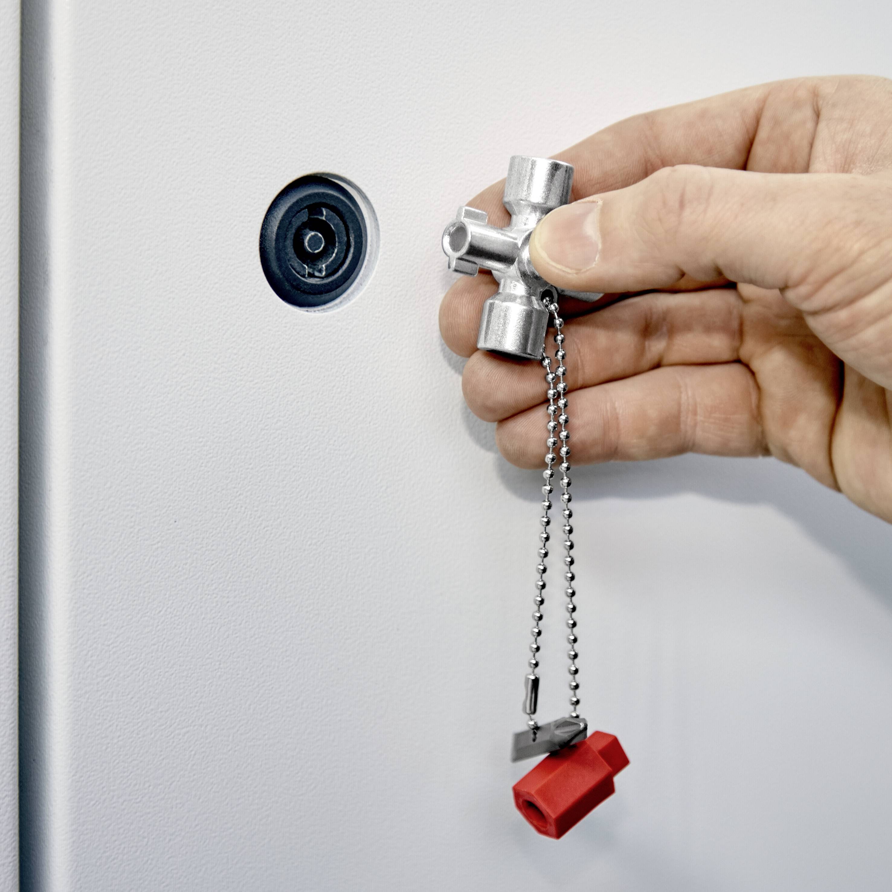 Eine Hand dreht einen Sicherheitsschlüssel im Schloss eines weißen Tresors. Ein roter Plastikdeckel hängt am Schlüsselkettchen.