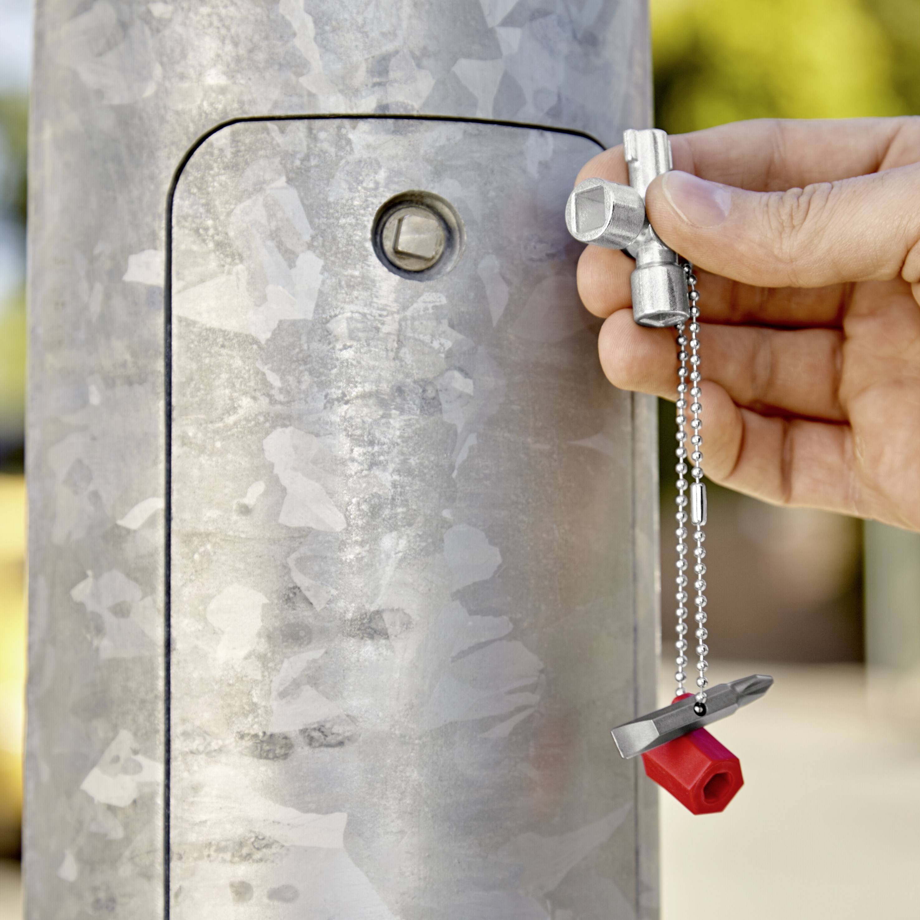 Eine Hand hält einen silbernen Schlüssel, der ein quadratisches Schloss an einem grauen Metallmast öffnet.