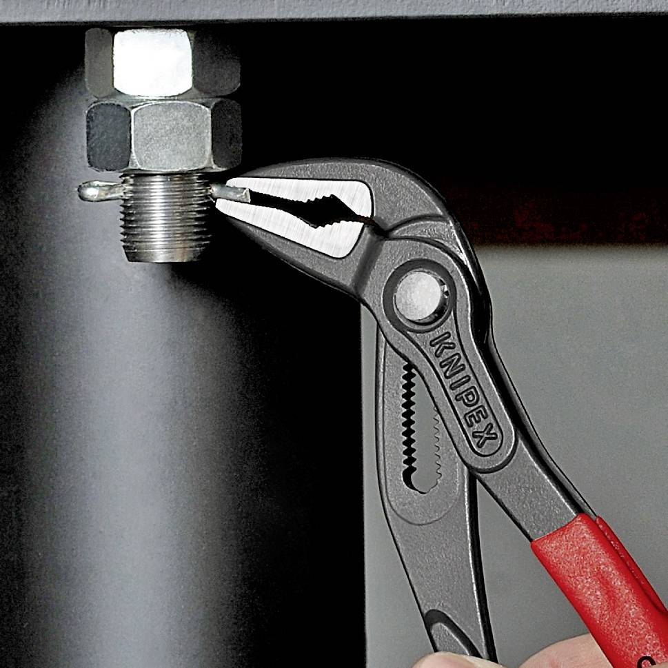 Eine Hand hält eine Wasserpumpenzange, die an einer Metallmutter befestigt ist. Die Zange greift fest und zeigt handwerkliche Tätigkeit.