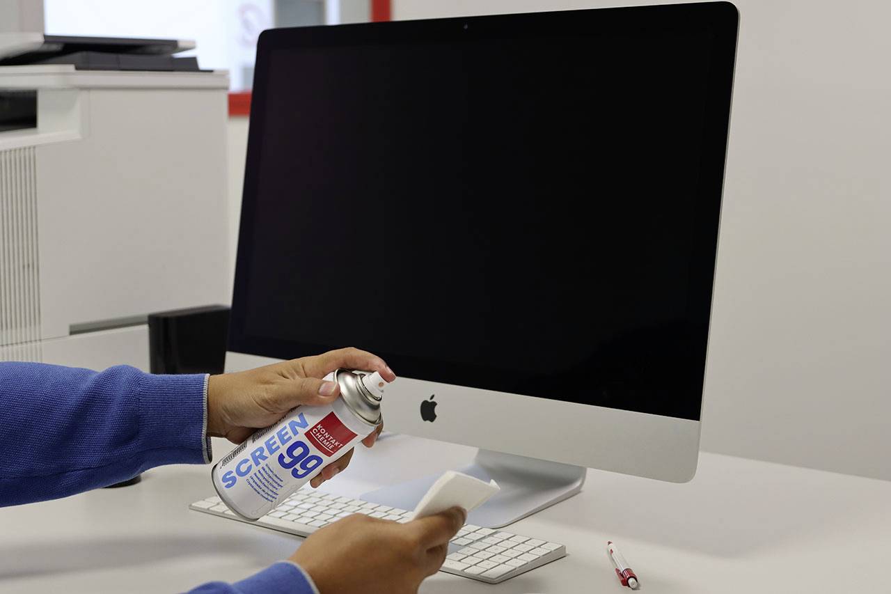 Eine Person reinigt den Bildschirm eines Computers mit einem Tuch und einem Bildschirmreiniger-Spray. Der Bildschirm ist schwarz.