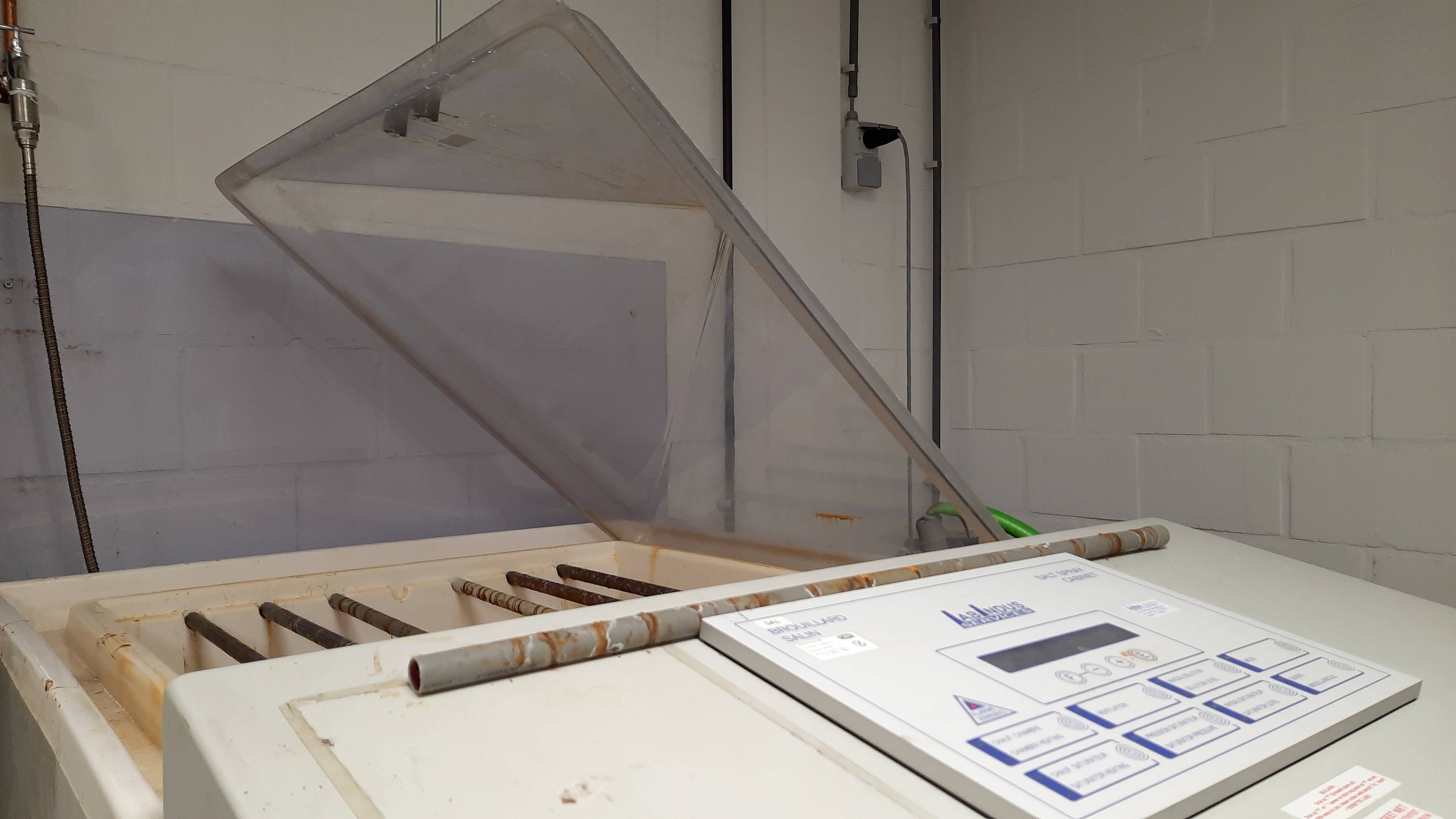 Ein Wäschetrockner in Industrielook mit offenem Deckel und Bedienfeld. Umgebung zeigt weiße Wände und Rohre.