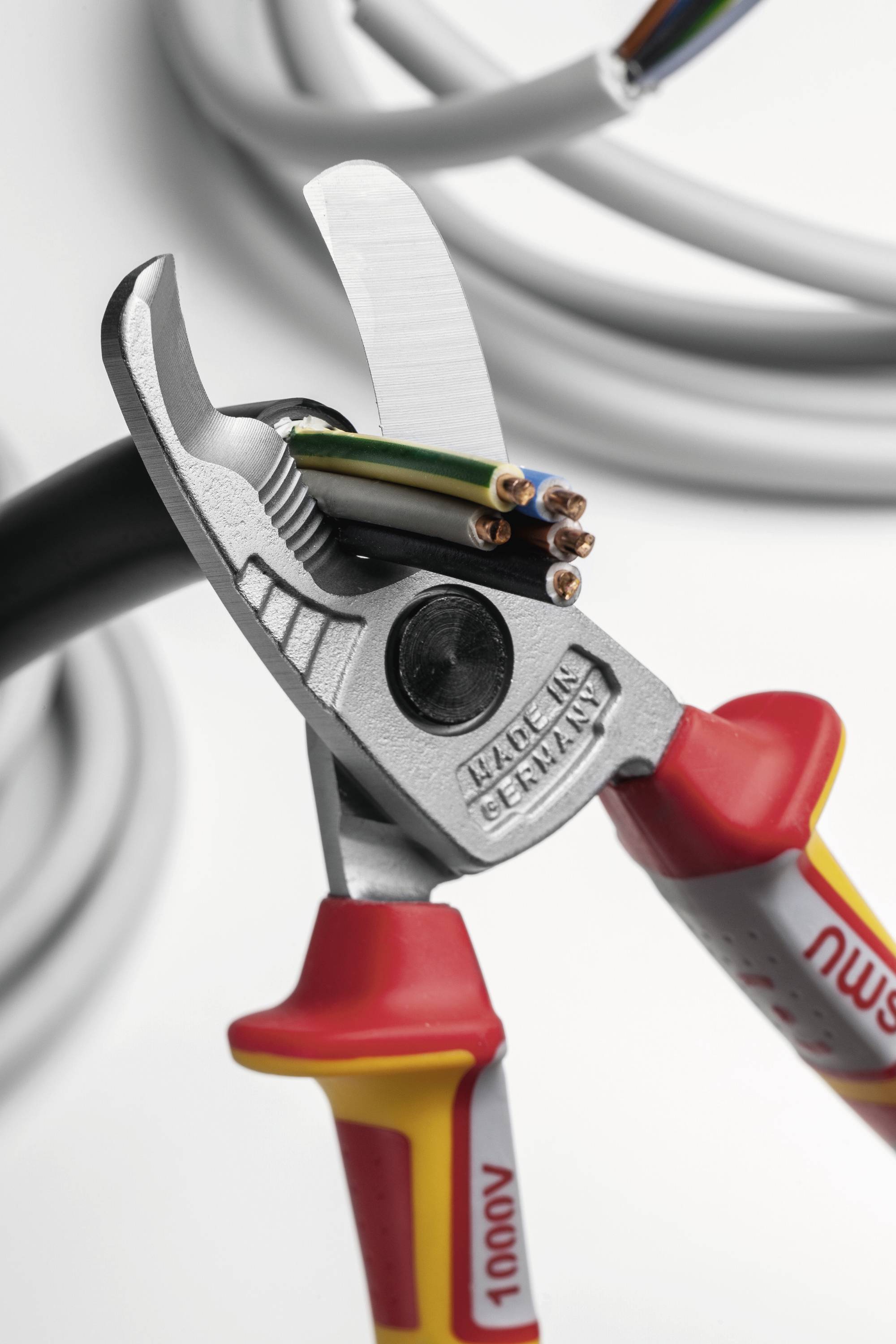 Isolierte Drahtschneider, die ein dickes Elektrokabel durchtrennen und dabei die mehrfarbigen Drähte im Inneren freilegen, was eine sichere Handhabung von stromführenden Leitungen signalisiert.