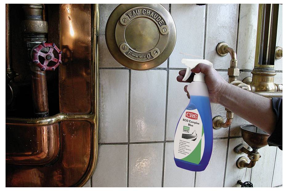 Eine Hand hält eine CRC ECO Complex Reinigungsspray-Flasche in der Nähe von industrieller Rohrleitungsanlage und deutet auf deren Verwendung zum Reinigen von Rohren oder Ausrüstung hin.