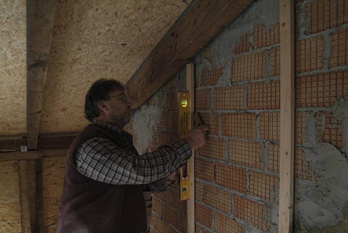 Ein Mann verwendet eine Wasserwaage und einen Bleistift, um eine Backsteinwand zu vermessen und auszurichten.