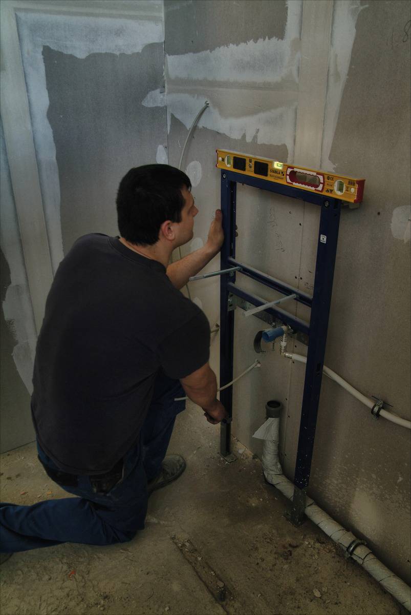Eine Person installiert ein Sanitärgestell an einer Wand, während sie mit einer Wasserwaage die Ausrichtung überprüft.