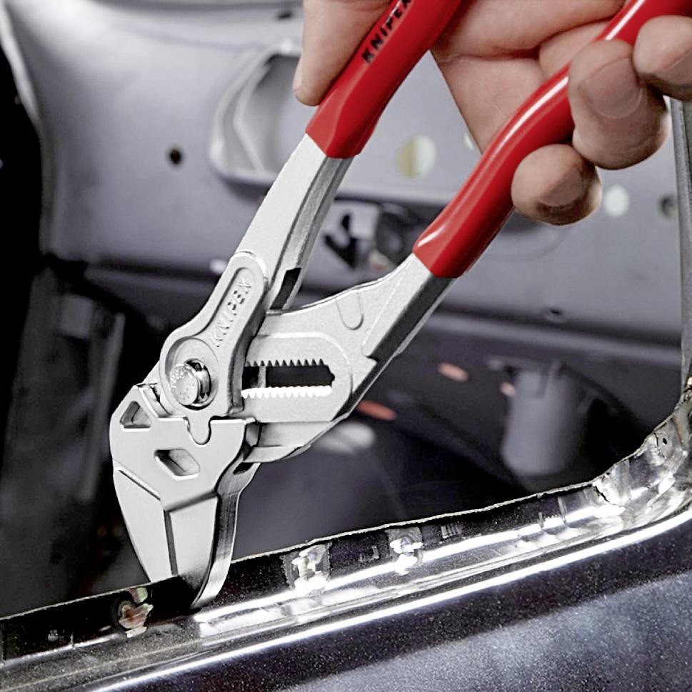 Eine Hand hält eine verstellbare Zange, die ein Metallobjekt in einer Werkstatt oder Fabrikumgebung greift.