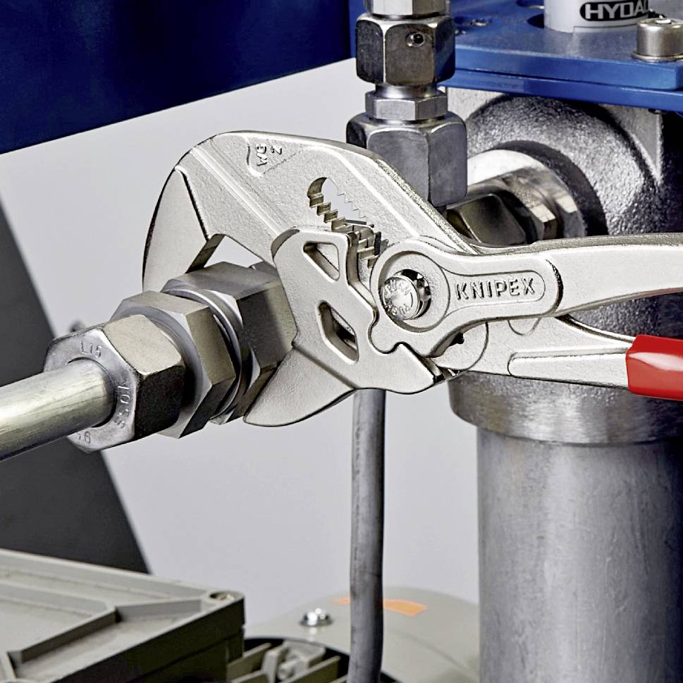 Eine Rohrzange hält eine Metallmutter an einem Rohr fest. Die Zange zeigt die Marke 'KNIPEX'. Im Hintergrund sind Maschinenbestandteile zu sehen.
