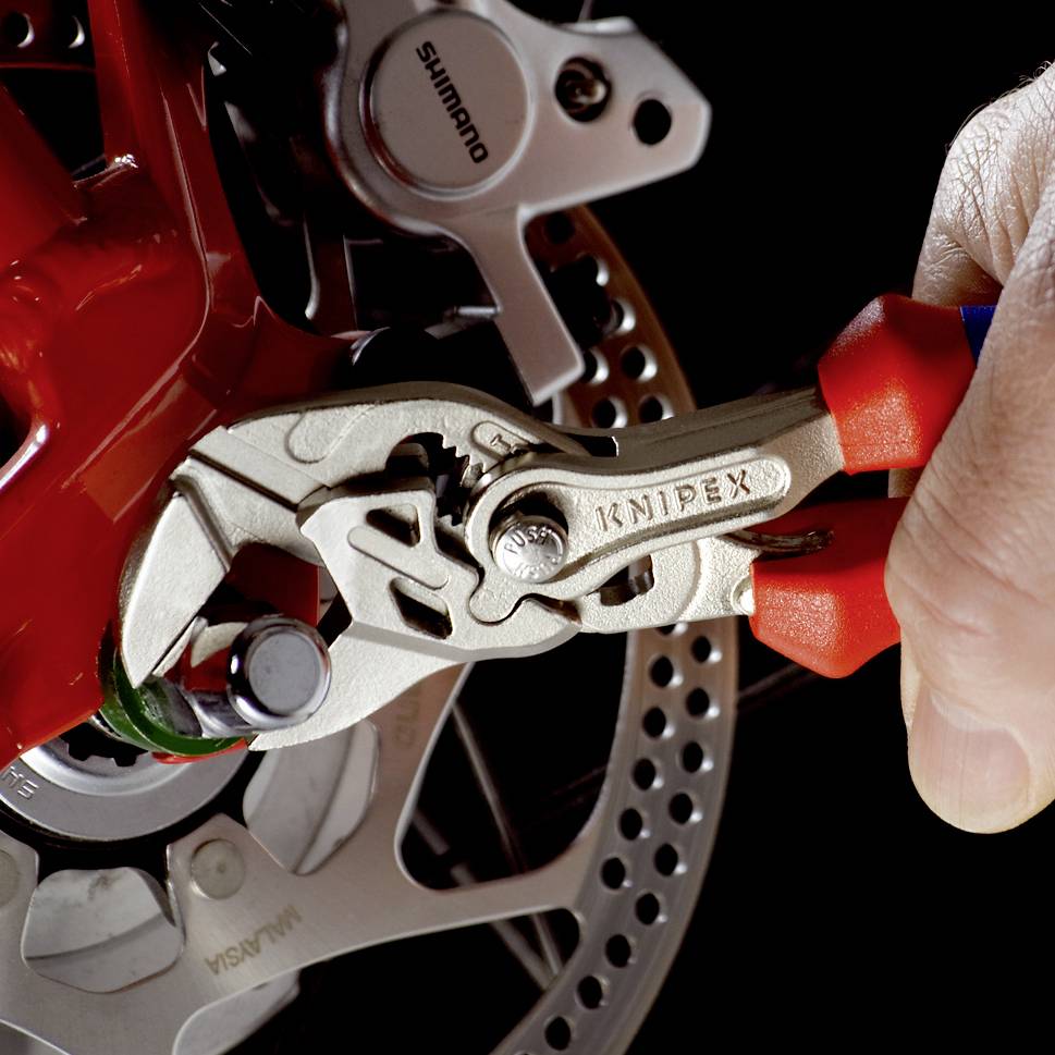 Eine Hand hält eine Knipex-Zange und justiert eine Fahrrad-Scheibenbremse.