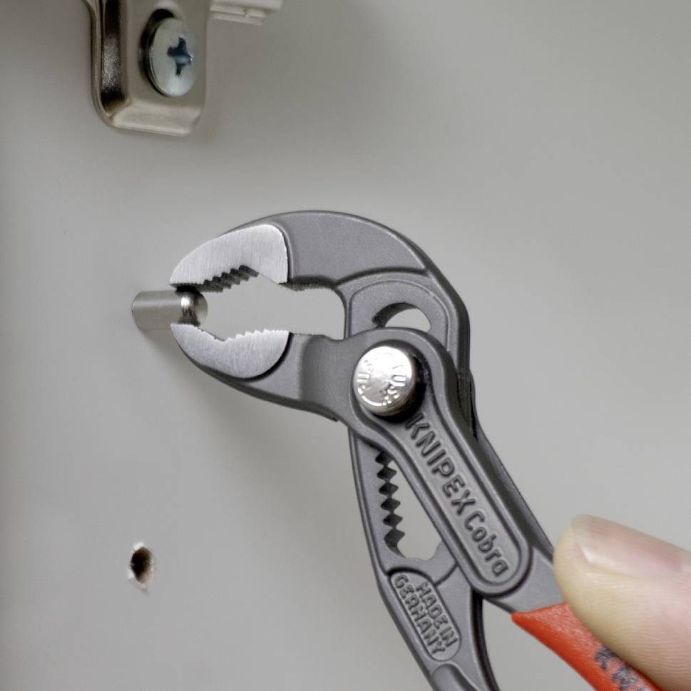 Eine Hand hält eine Wasserpumpenzange, die eine Schraube an einem Metallteil anzieht. Die Zange ist von der Marke KNIPEX Cobra.