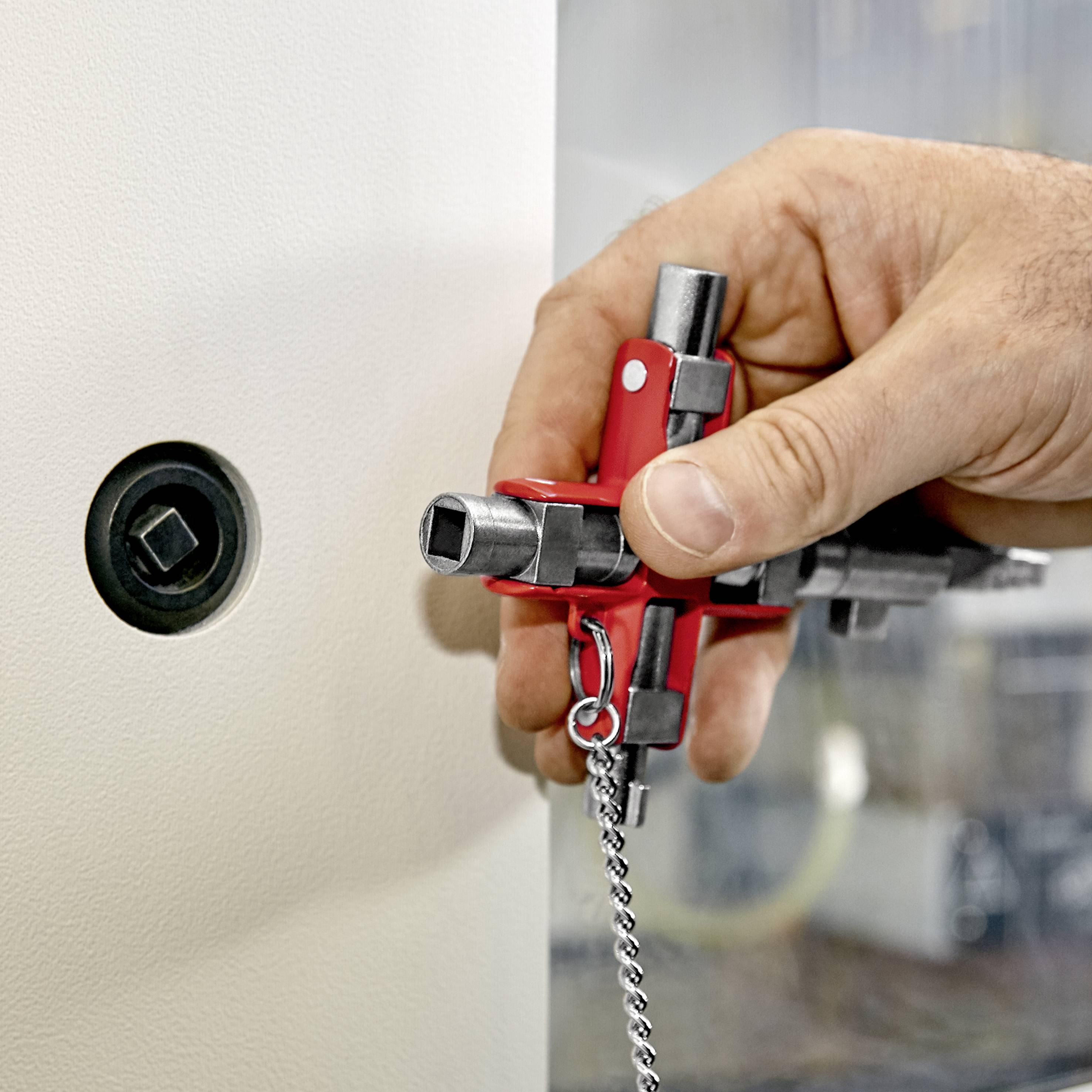 Eine geöffnete Schranktür wird mit einem Vierkantschlüssel von einer Hand bedient, während das Schloss sichtbar ist.