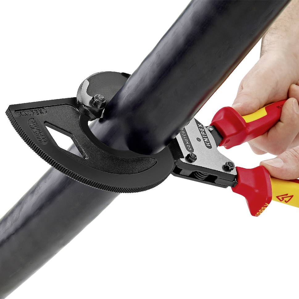 Hand hält ein Kabelschneider-Werkzeug, das ein dickes schwarzes Kabel schneidet. Das Werkzeug hat rote und gelbe Griffe.