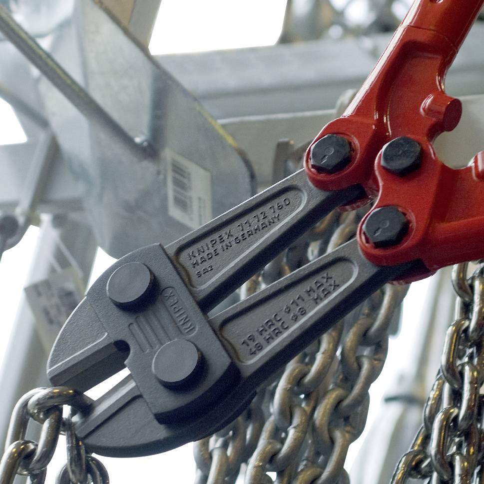 Eine rote Bolzenschneiderzange schneidet eine Metallkette. Werkzeuge im Hintergrund.