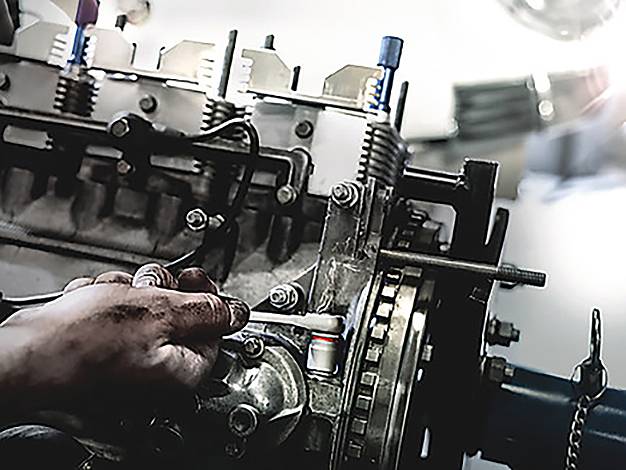 Eine Person arbeitet an einem Automotor und zieht Schrauben mit einem Schraubenschlüssel fest. Der Motor ist detailliert und zeigt verschiedene Komponenten und metallische Teile.