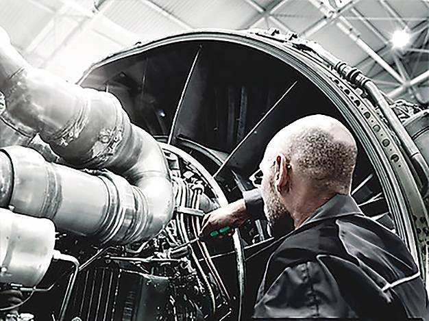 Eine Person in einer Werkstatt untersucht die komplizierten Teile eines großen Motors, was auf technische Wartung oder Ingenieurarbeit hindeutet.