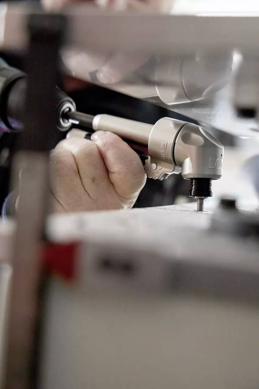 Eine Person nutzt ein Präzisionswerkzeug zur Einstellung von Maschinen und konzentriert sich intensiv. Die Umgebung wirkt industriell und betont sorgfältige Handwerkskunst.