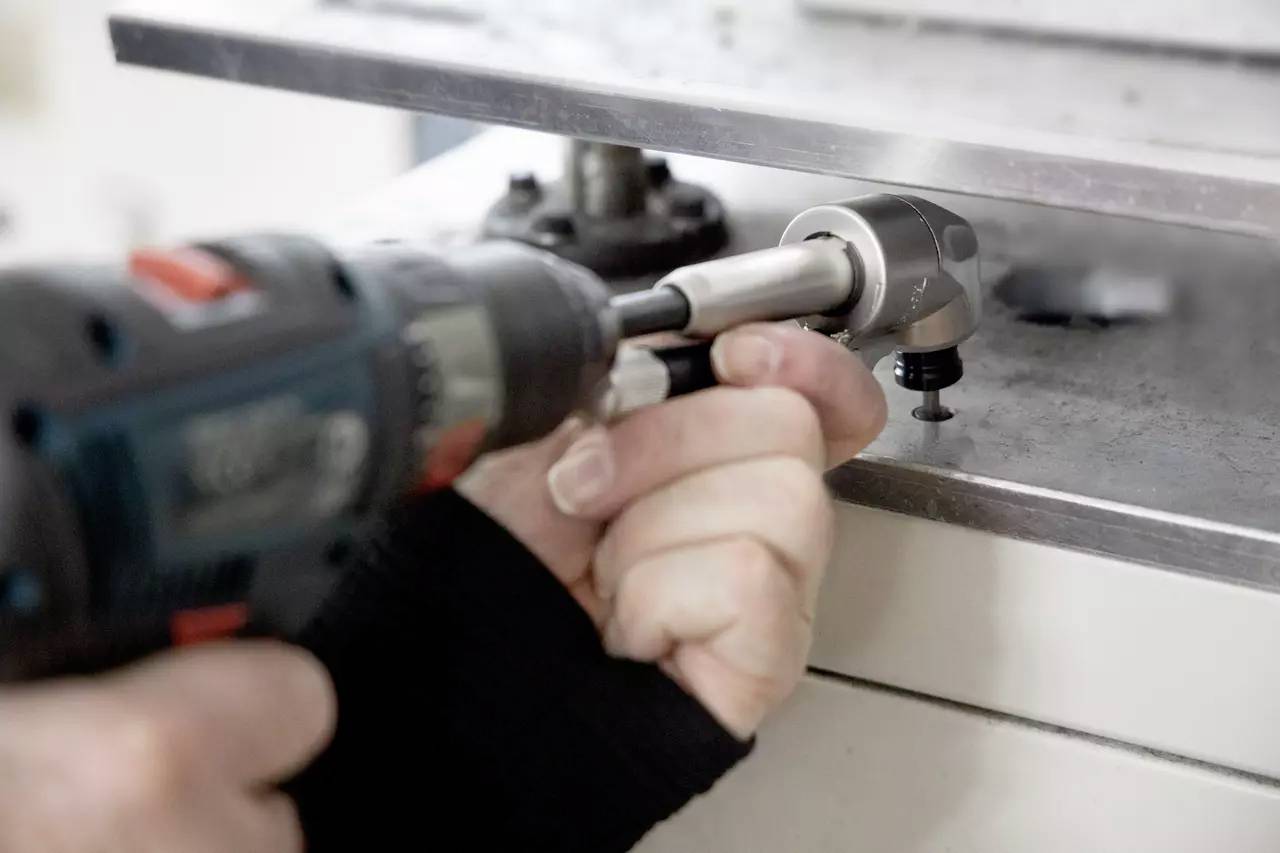 Eine Person, die eine Elektrobohrmaschine verwendet, um eine Metallkomponente auf einer Werkbank zu justieren oder zu montieren.