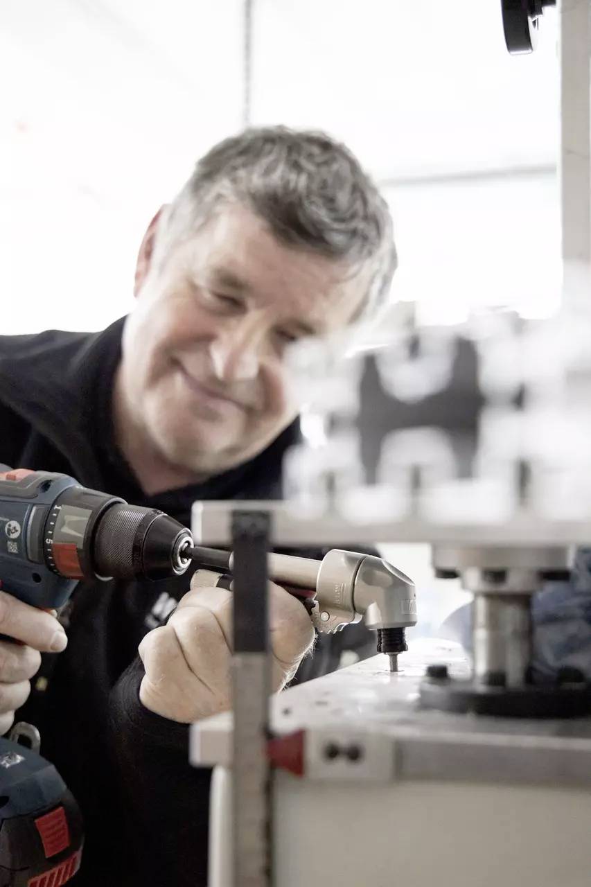 Ein Mann konzentriert sich auf die Verwendung einer Elektrobohrmaschine an Maschinen und zeigt handwerkliche Arbeiten in einer Werkstattsumgebung.