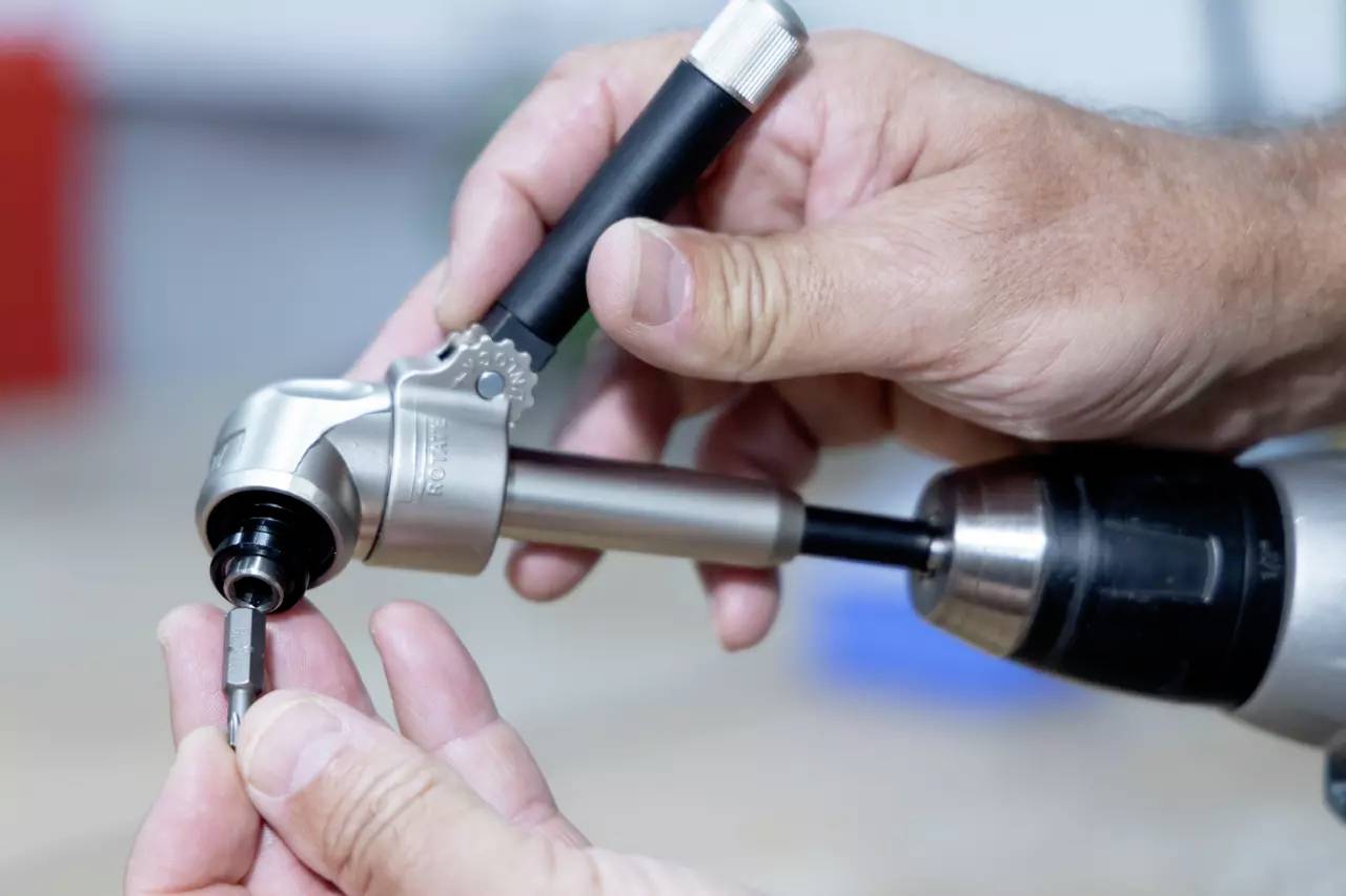 Hände, die einen Bohrer mit einer Winkelaufsätze bedienen, demonstrieren ein Werkzeug in Aktion.